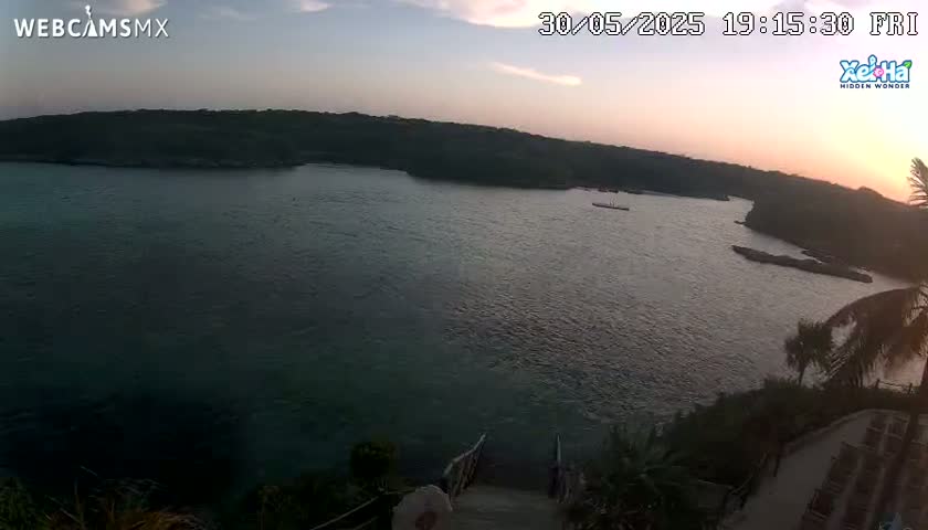 A tranquil sunset over a calm bay, nestled between dark green hills, with a set of stairs leading down to the water.