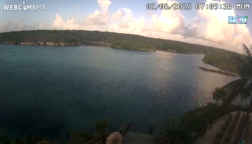 A partly cloudy morning reveals a tranquil body of water surrounded by lush green vegetation, viewed from a high vantage point overlooking a staircase leading down to the water's edge.