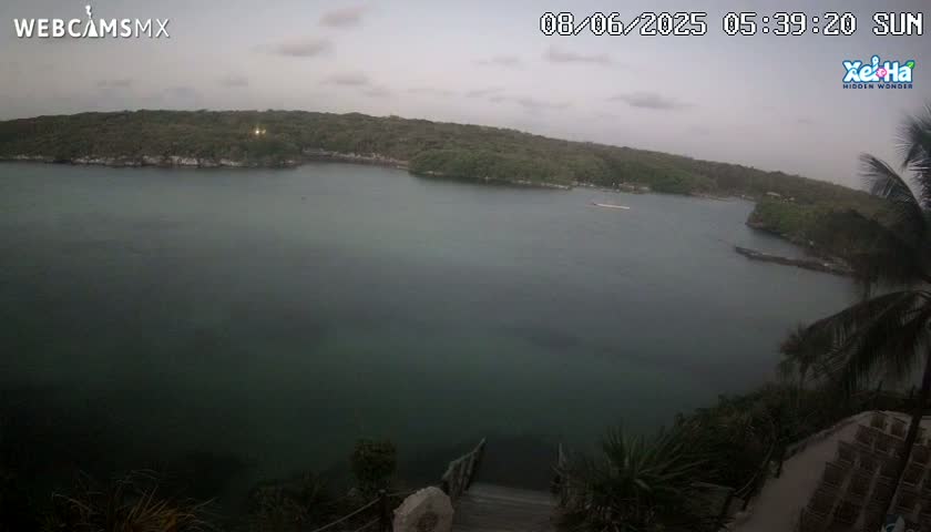 A calm, overcast day shows a tranquil bay nestled between lush green hillsides, with a stairway descending toward the water's edge.