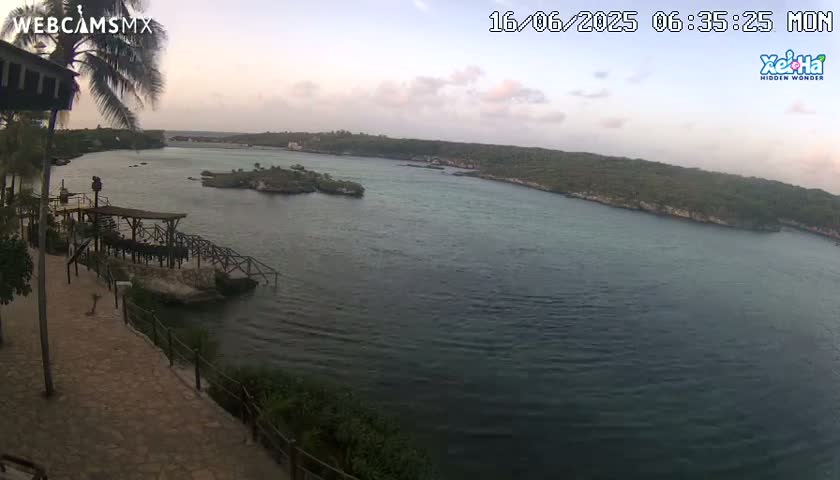 A tranquil cove with calm water under a partly cloudy, dusky sky is viewed from an elevated vantage point near a waterfront structure.