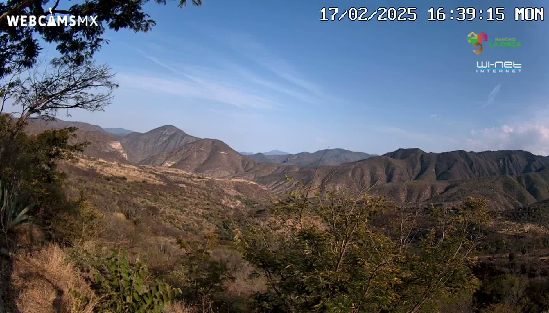A mostly clear blue sky overlooks a dry, mountainous landscape with brown and sparsely vegetated hills and valleys.