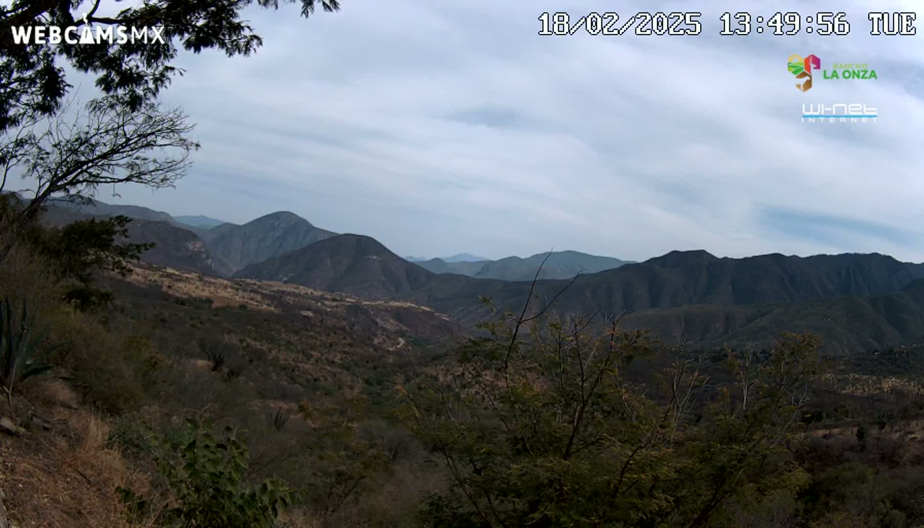 A view of a mountainous landscape under a mostly cloudy sky shows a valley with sparse vegetation.