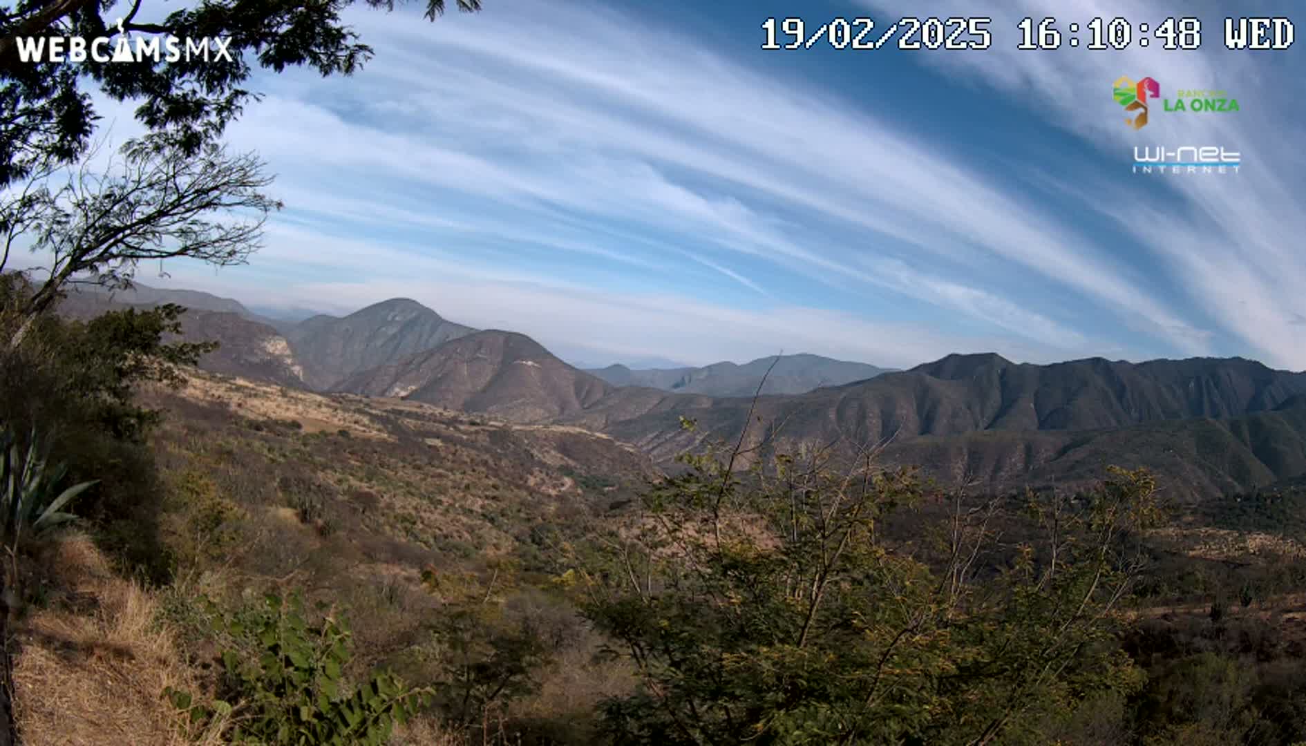 A panoramic view of a mountainous landscape under a partly cloudy sky shows brown hills and scrubby vegetation.