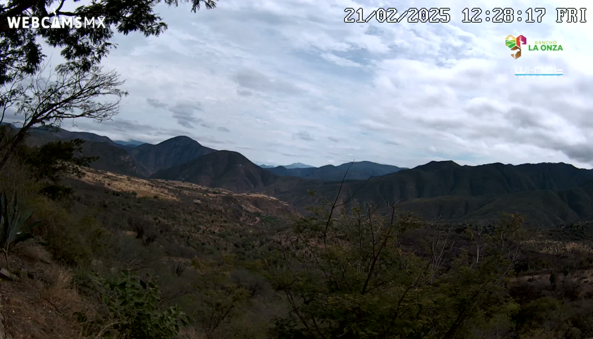 A view of a mountainous landscape under a cloudy sky shows a valley with sparse vegetation.