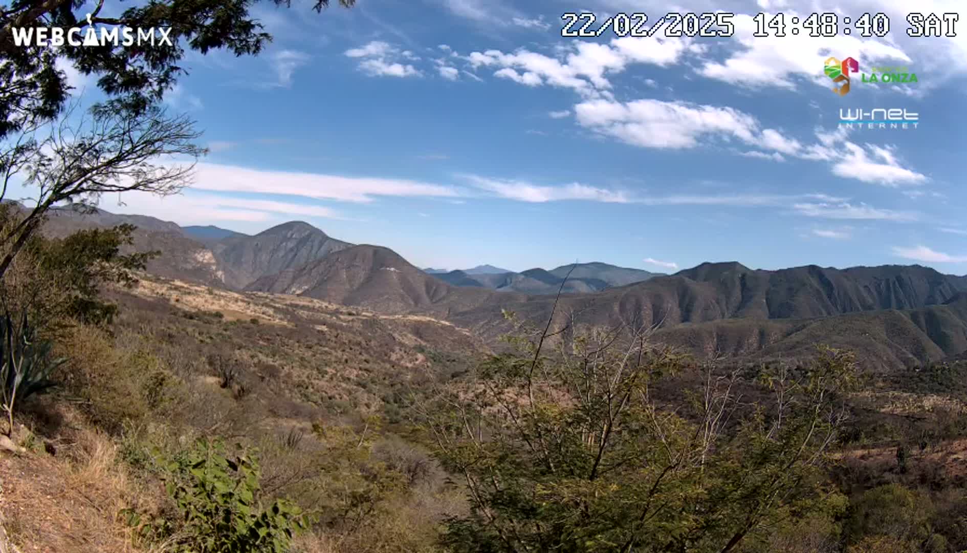 A mountainous landscape with scrubby vegetation under a partly cloudy blue sky.