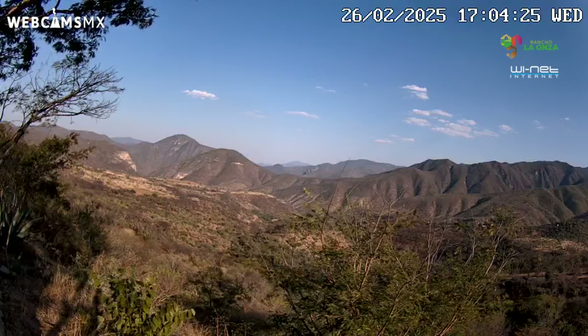 A mostly sunny, expansive view of dry, mountainous terrain with sparse vegetation.