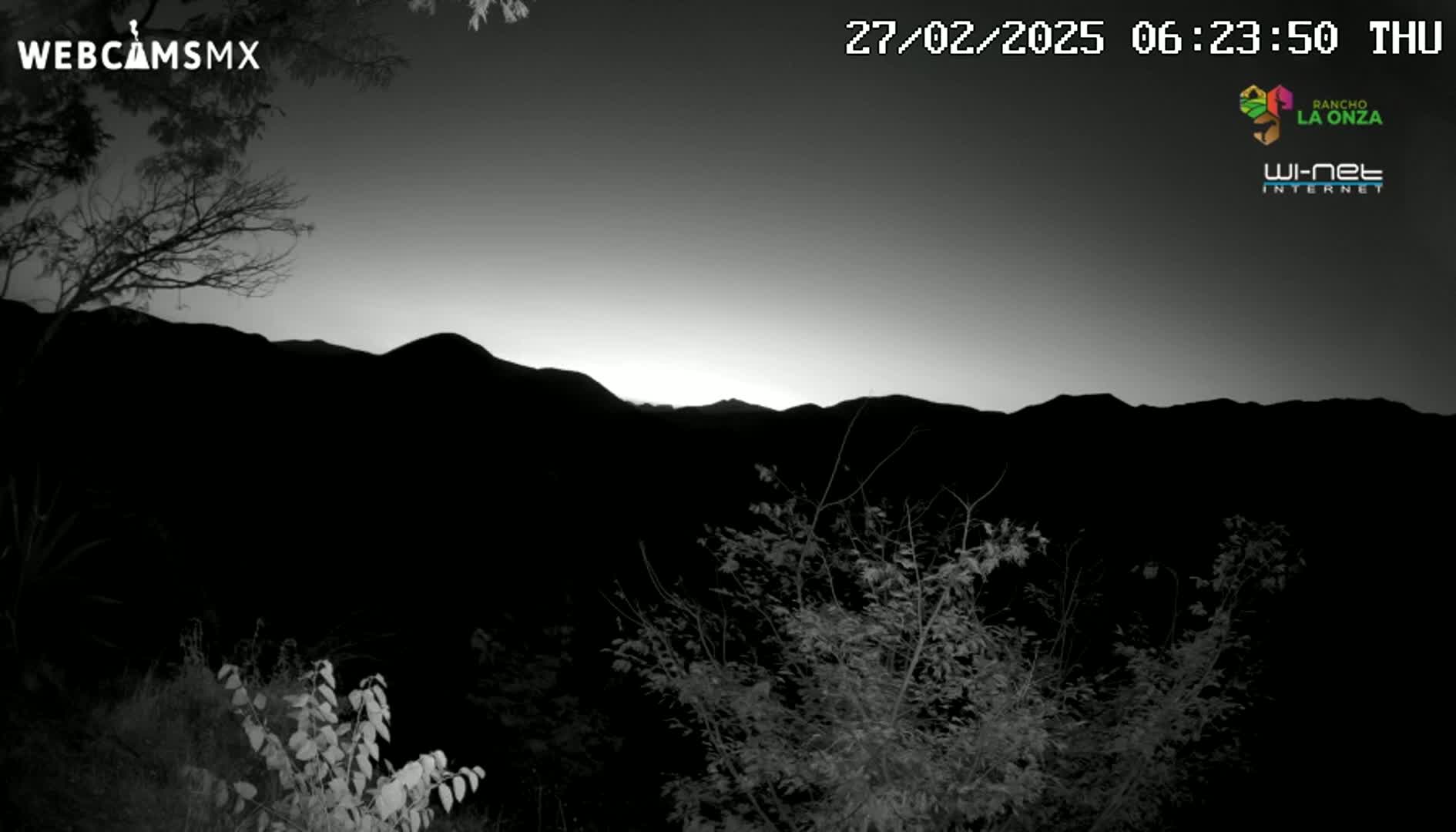 A dark, pre-dawn scene shows silhouetted mountains and trees under a light gray sky.