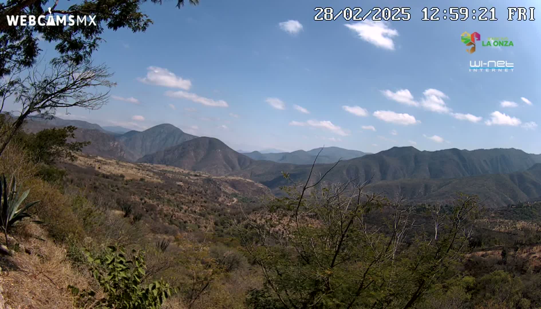A partly cloudy sky overlooks a dry, mountainous landscape with sparse, scrubby vegetation.