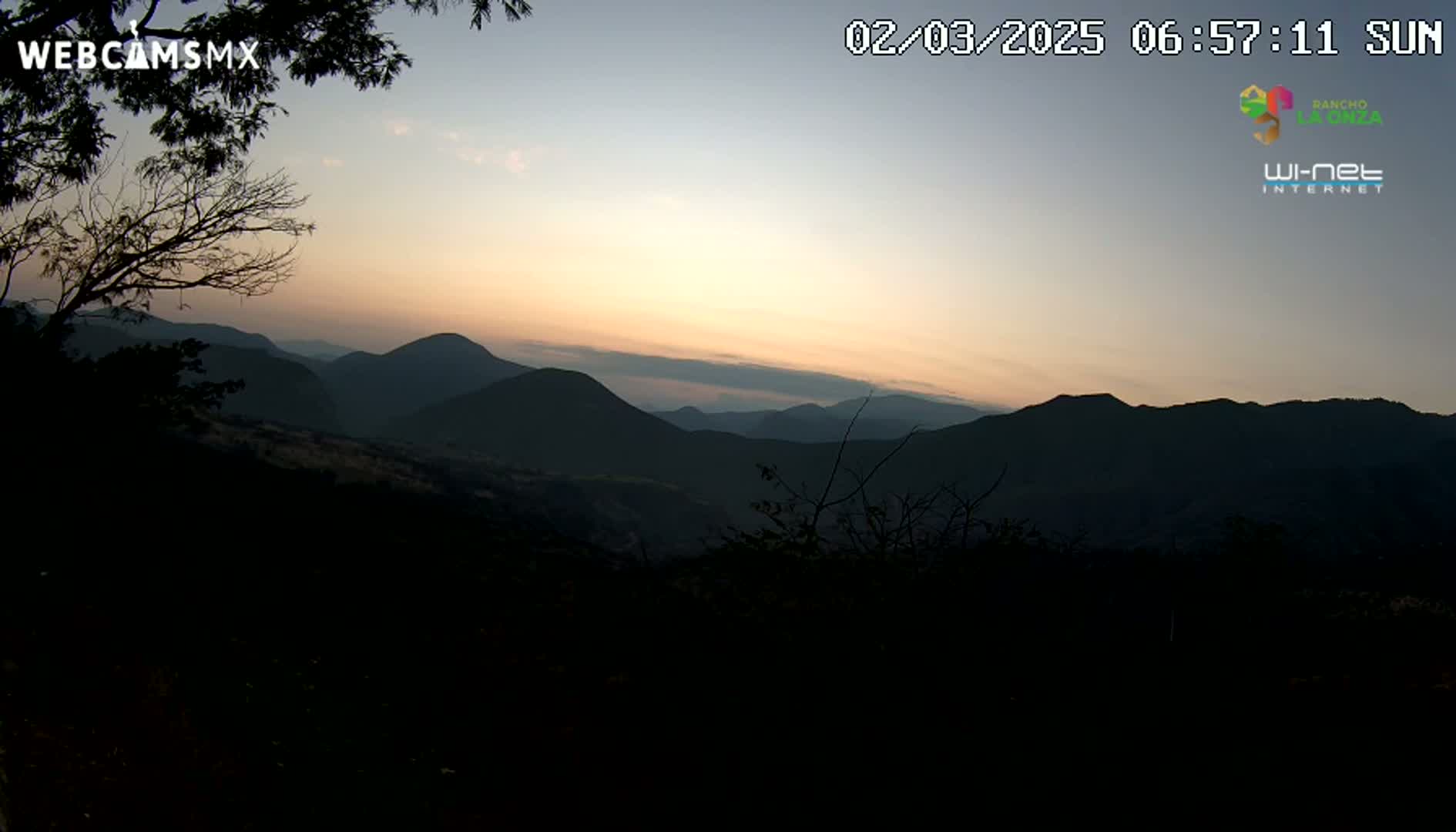 A sunrise illuminates a range of dark, silhouetted mountains.