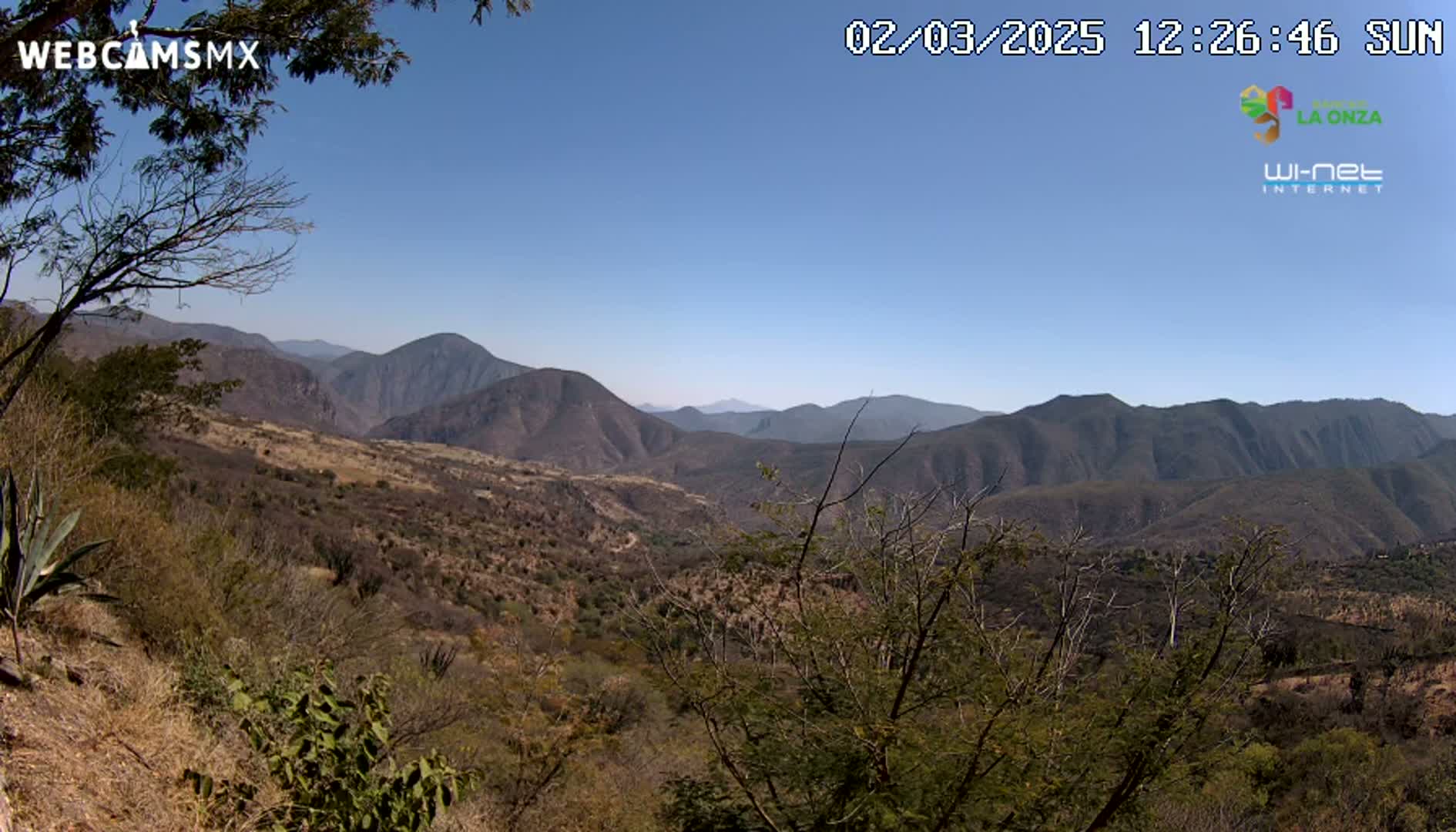 A sunny, clear day reveals a vast, mountainous landscape with sparse, dry-looking vegetation.