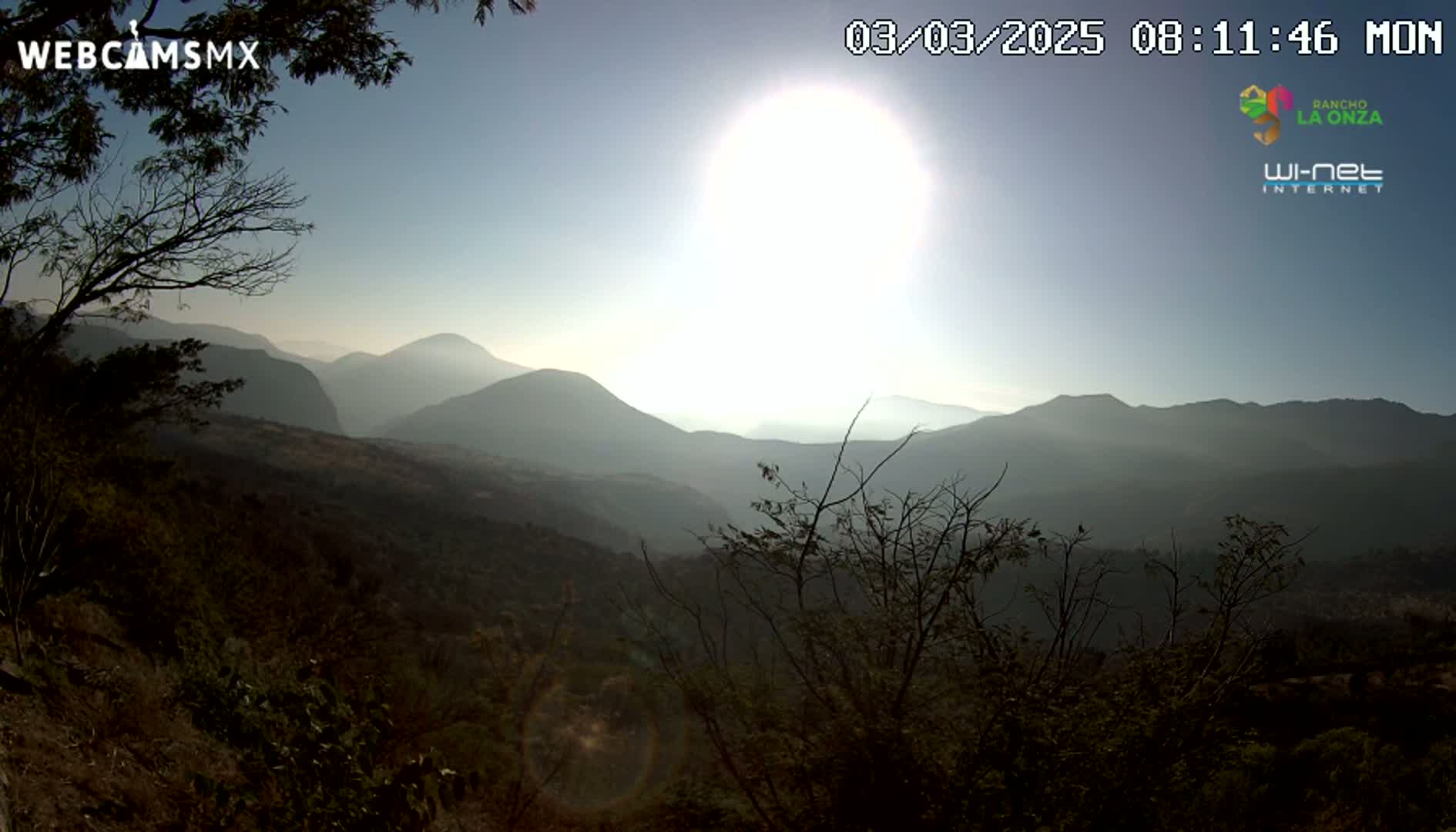 A bright sun shines over a hazy mountain range viewed from a high vantage point.