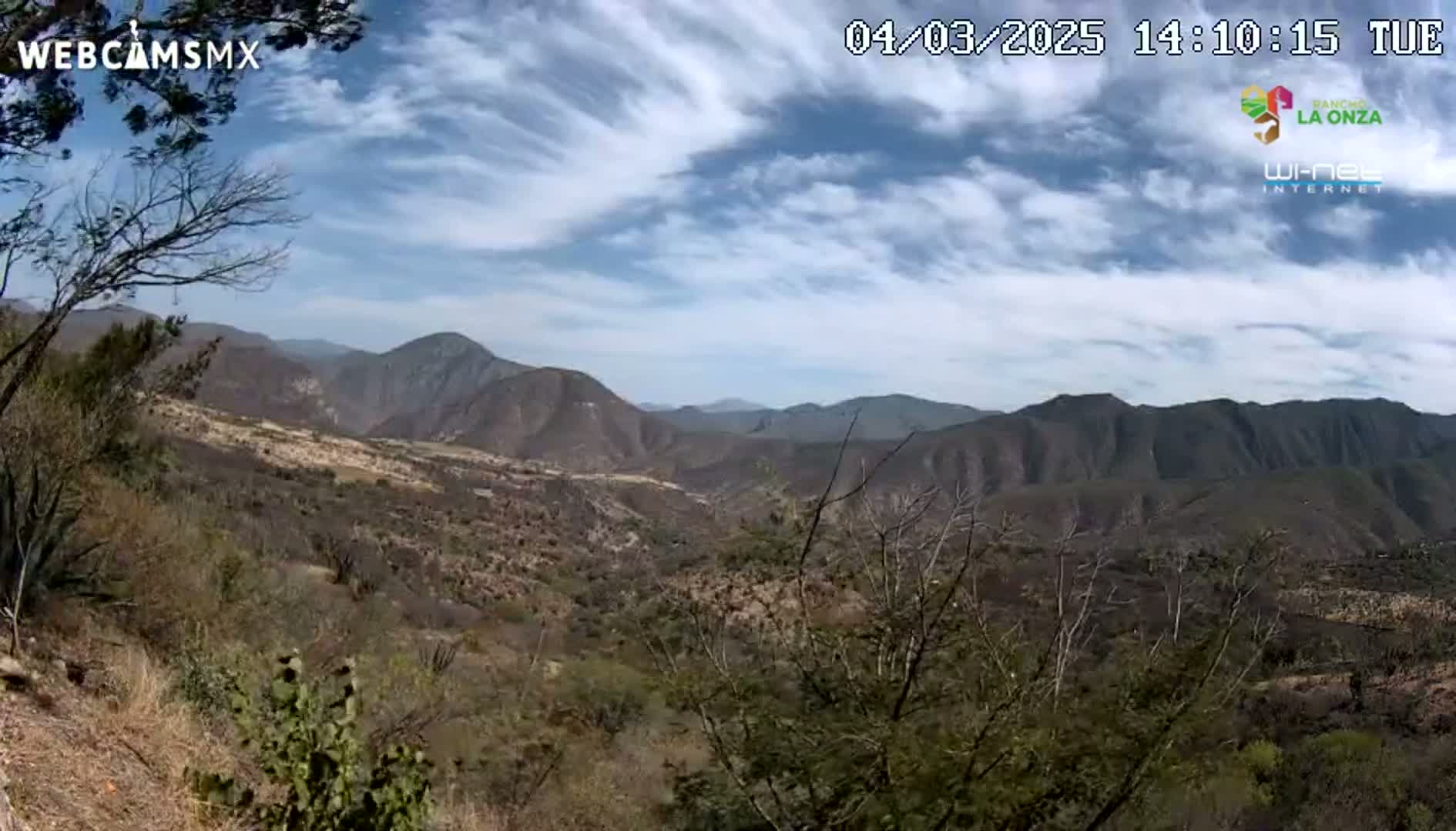 A partly cloudy sky overlooks a mountainous landscape with dry, brown vegetation.