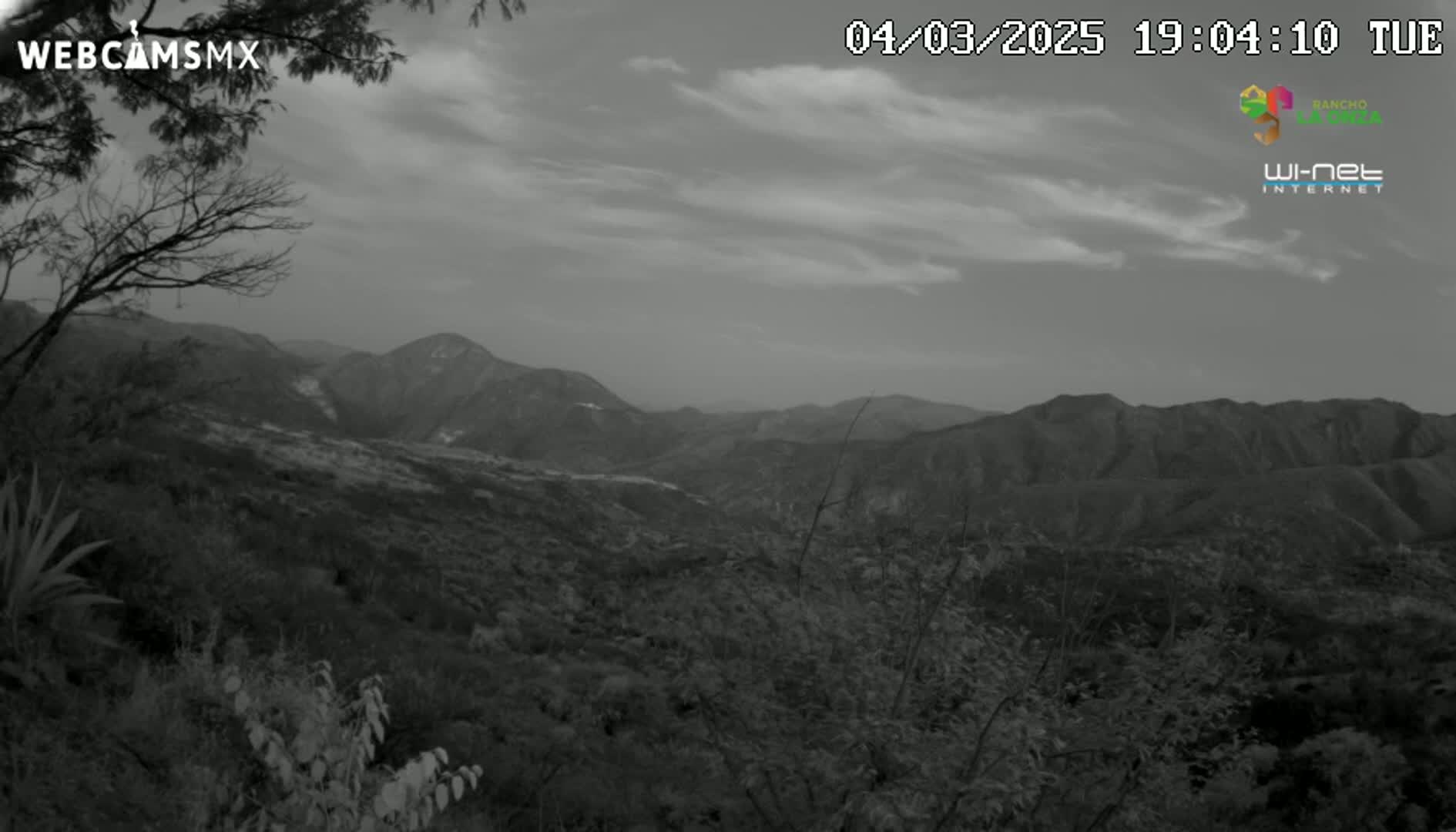 A grayscale view of a mountainous landscape under a partly cloudy sky.