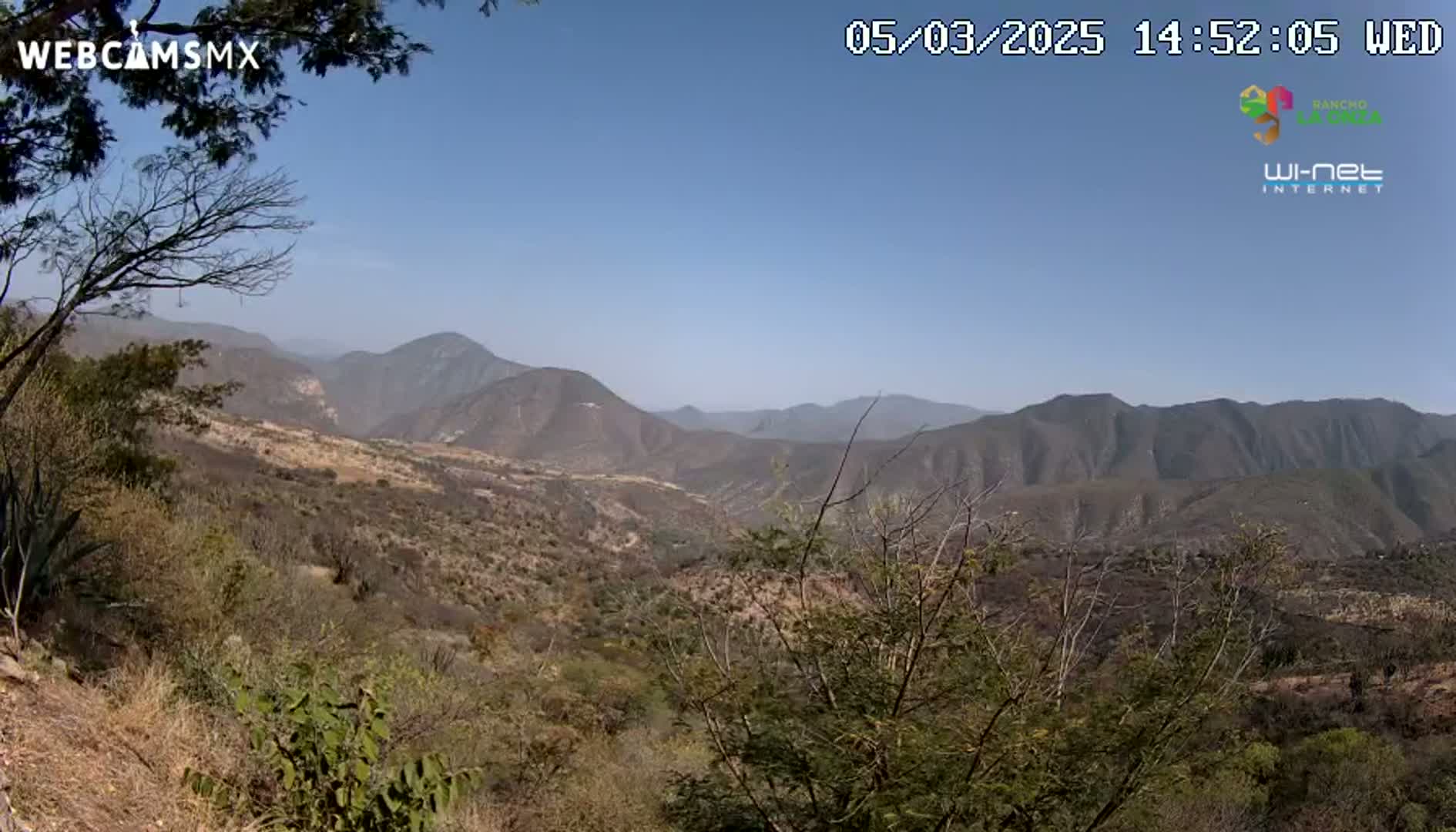 A panoramic view shows a vast, dry, mountainous landscape under a clear blue sky.