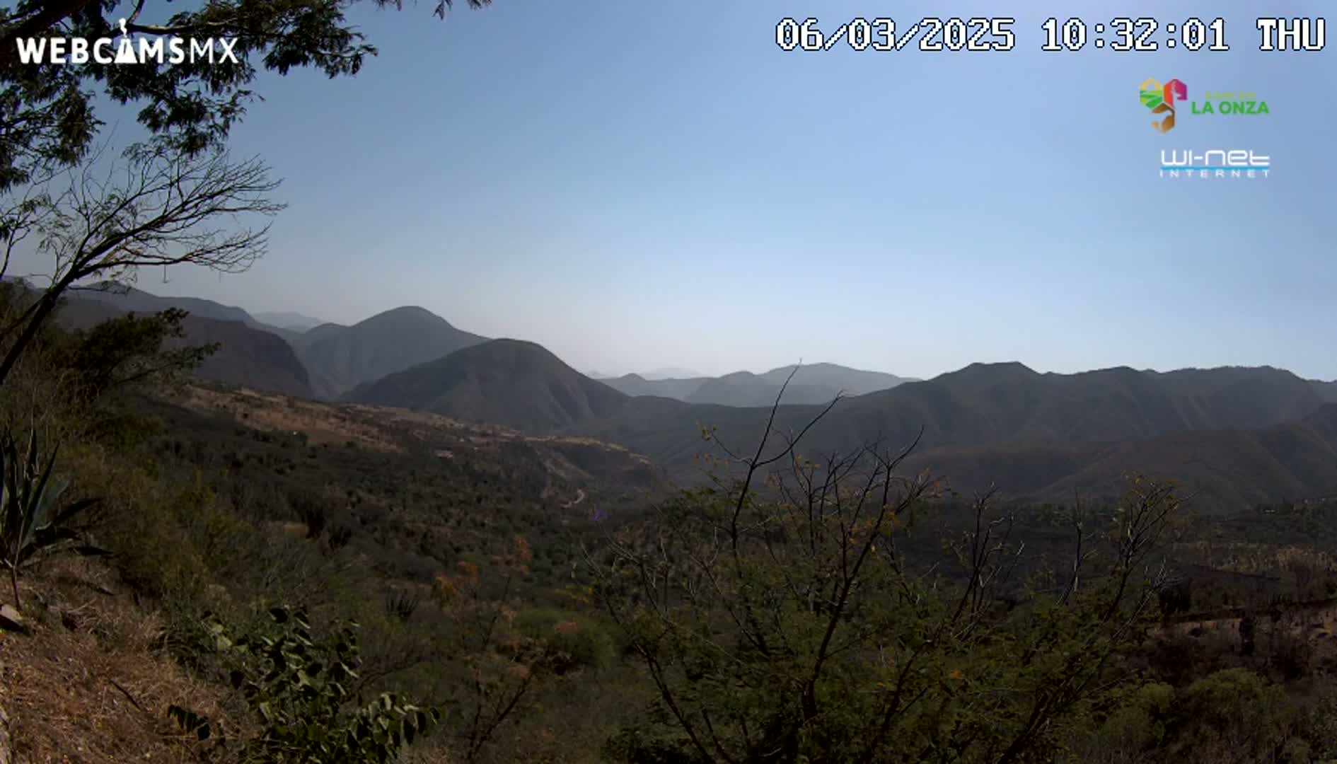 A view of a mountainous landscape under a clear blue sky shows scrubby vegetation covering the hills and valleys.