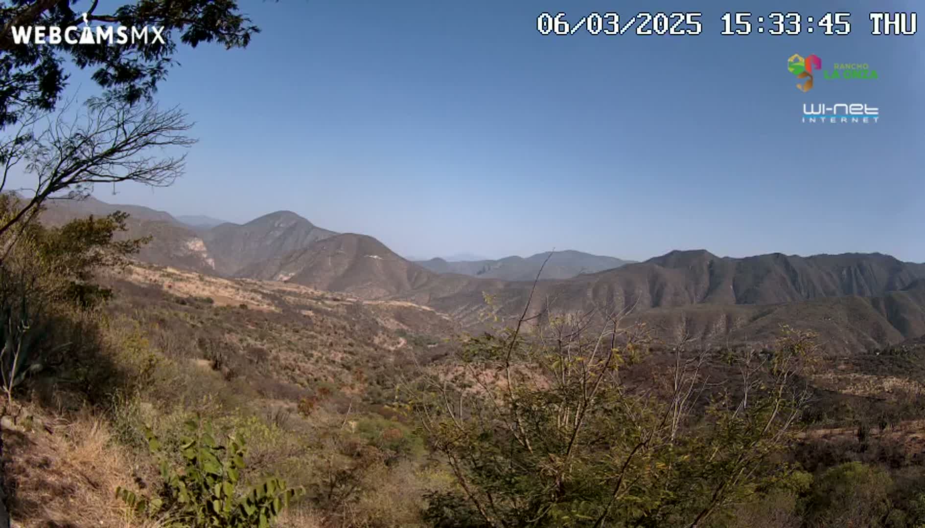 A high-angle view shows a dry, mountainous landscape under a clear blue sky.