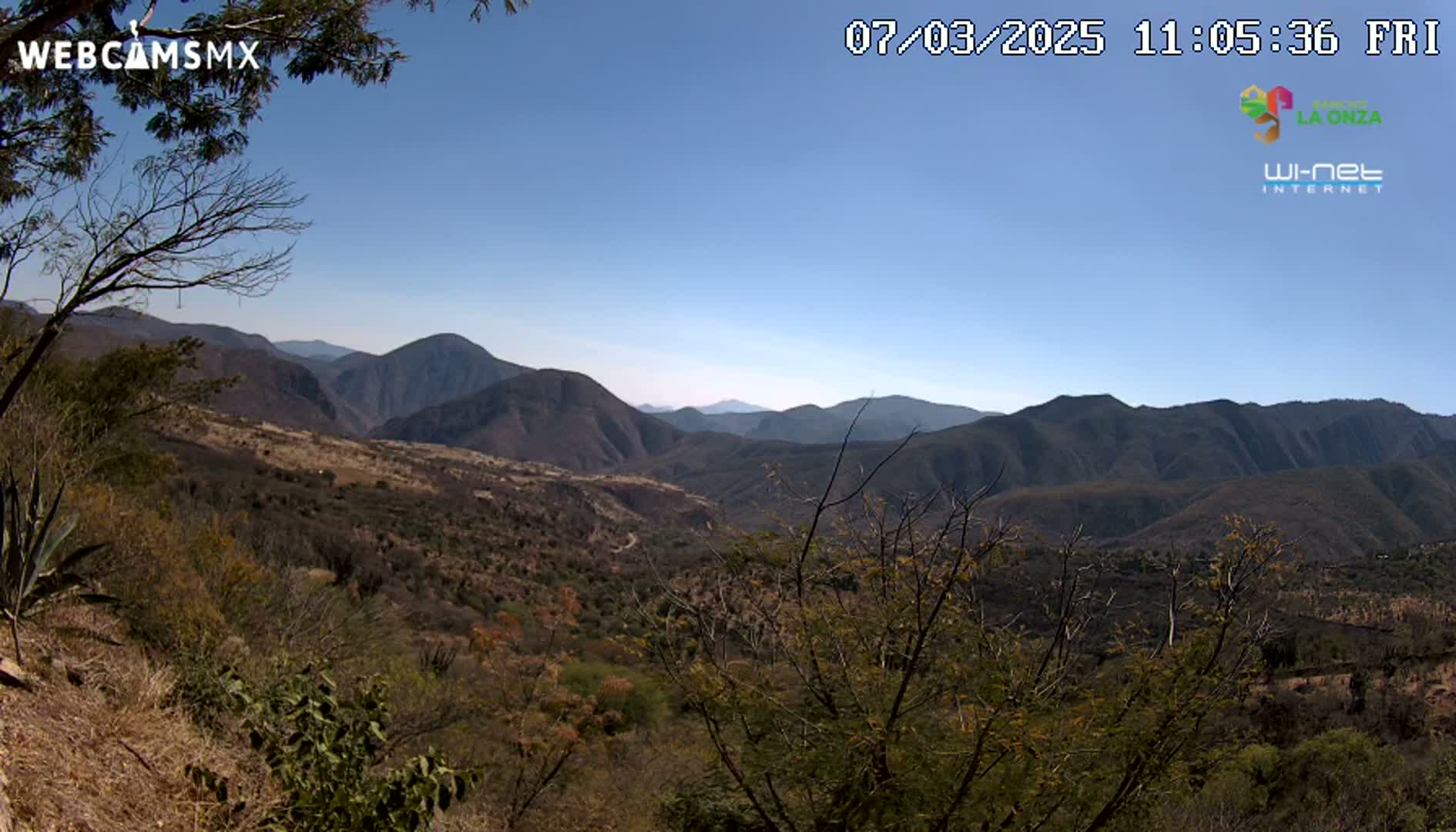 A clear, sunny day reveals a mountainous landscape with scrubby, brown vegetation covering the hills and valleys.