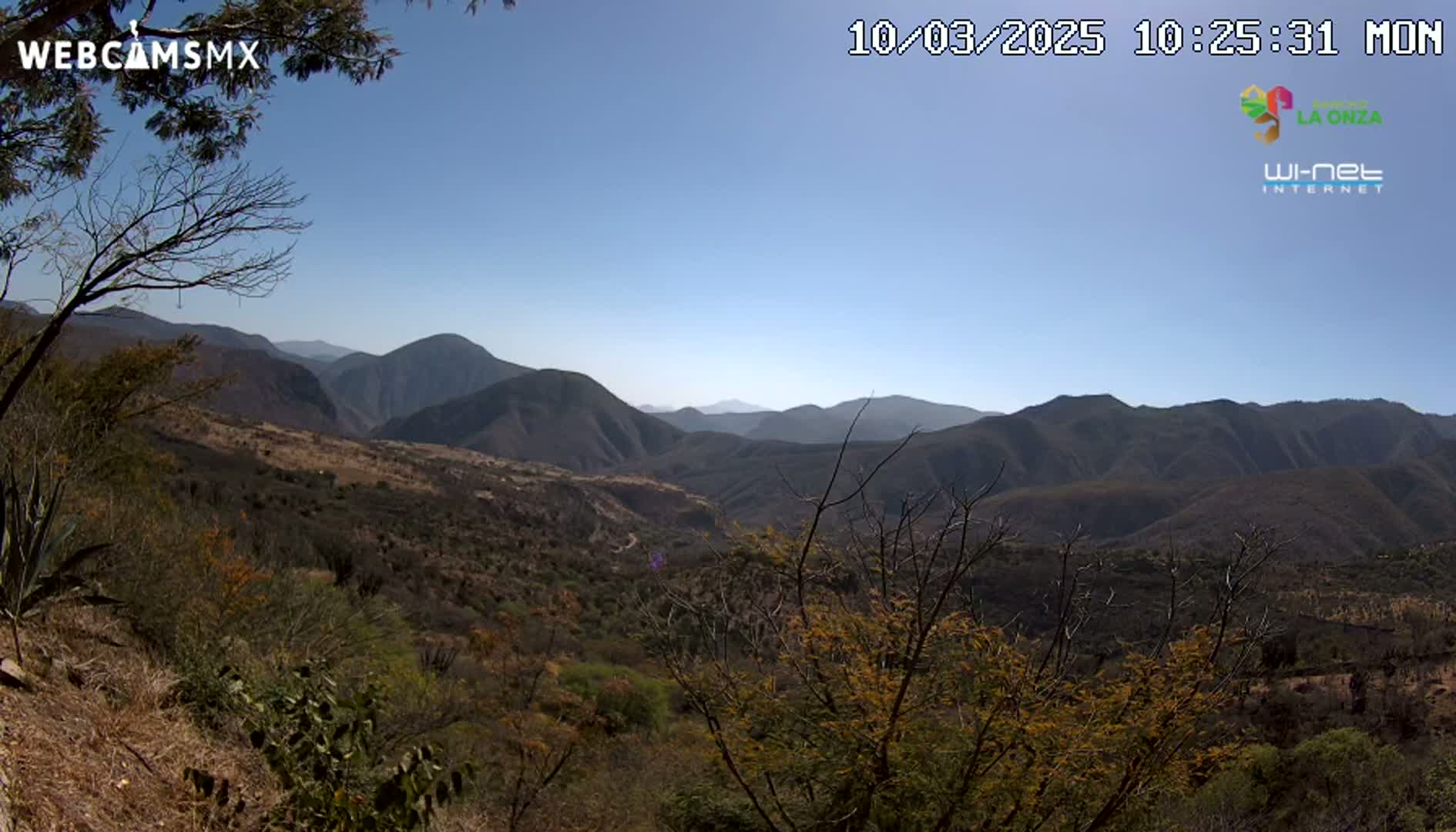 A view of a mountainous landscape under a clear blue sky shows dry, brown vegetation covering the hills and valleys.