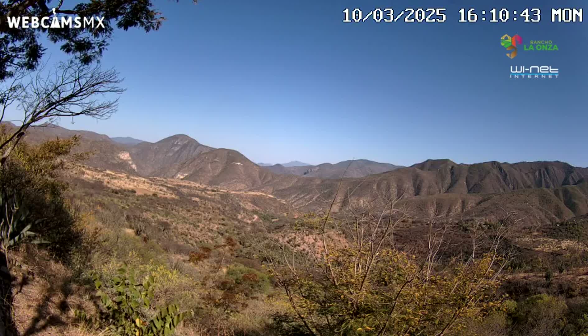 A mountainous landscape under a clear blue sky shows a dry, brown and sparsely vegetated valley extending to distant, rugged peaks.