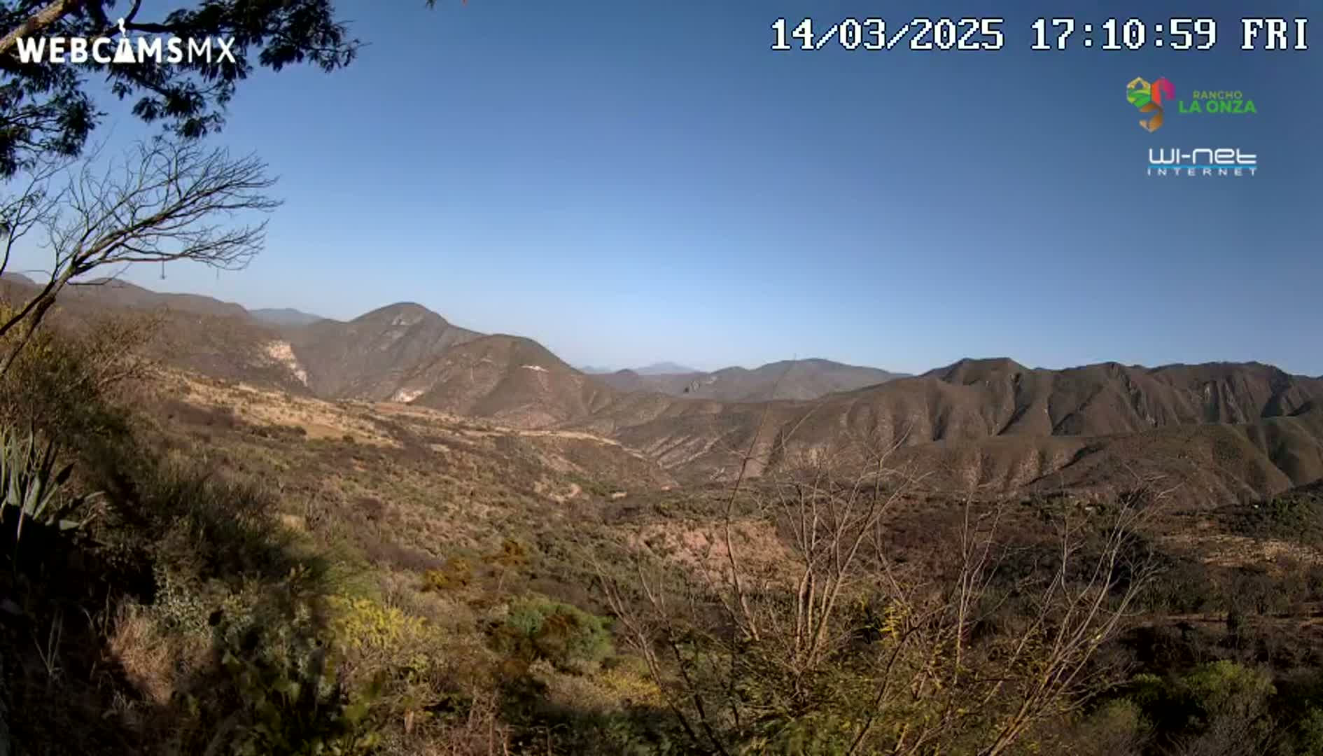 A high-angle view shows a vast, mountainous landscape under a clear blue sky, with dry, brown vegetation covering the hillsides.