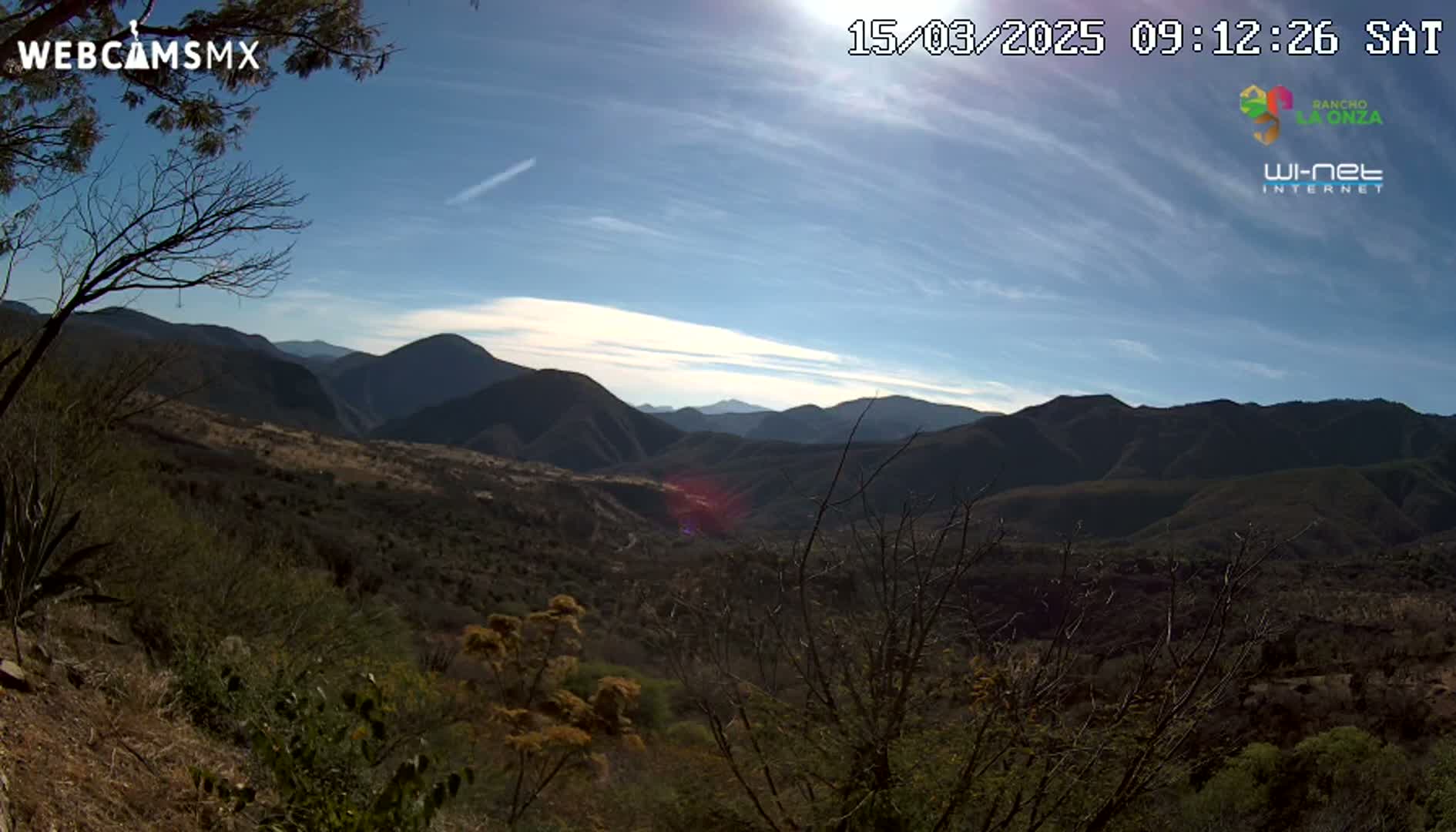 A sunny day reveals a vast mountainous landscape with scrub brush and trees covering the hillsides.