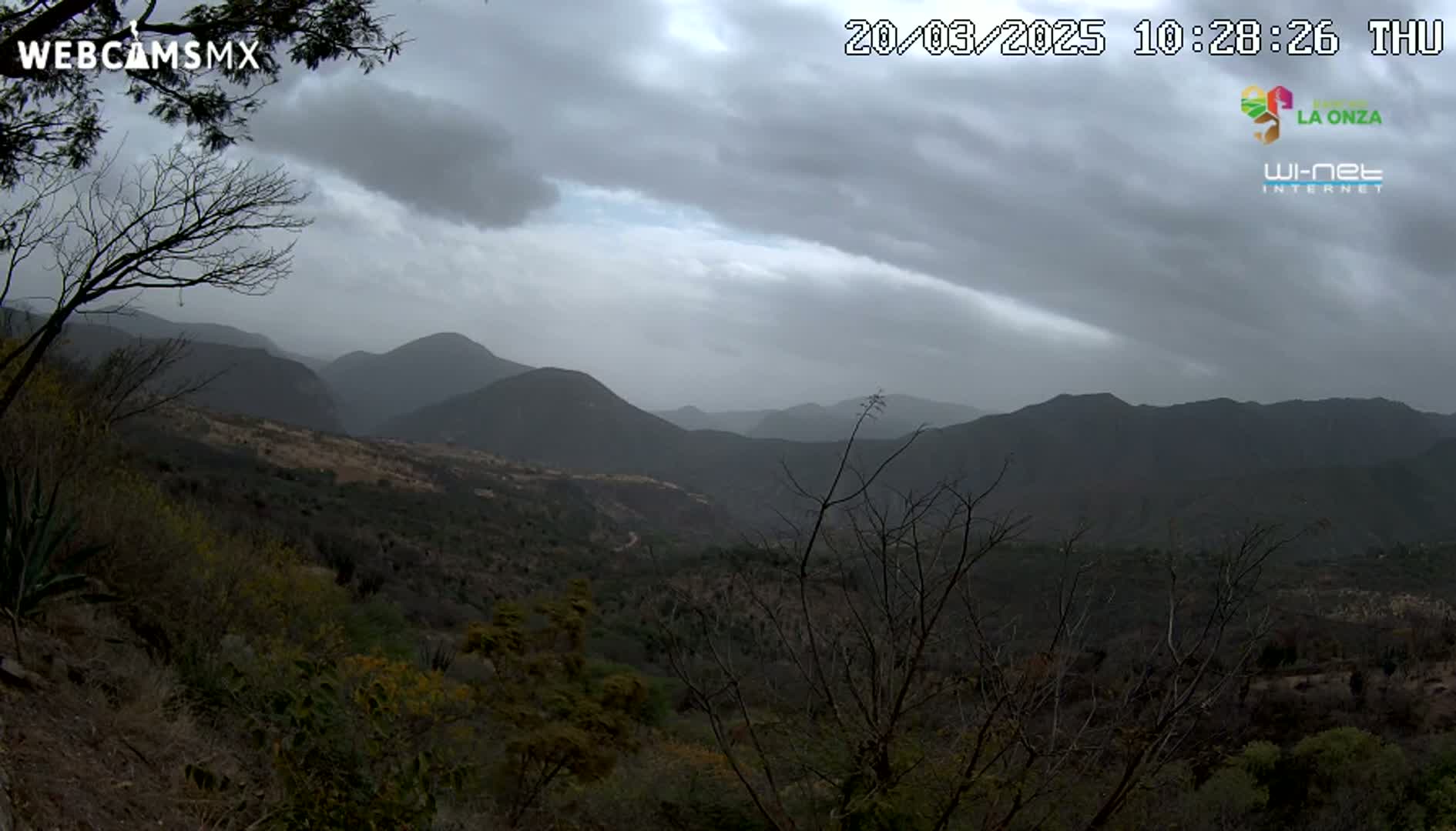 A view of a mountainous landscape under an overcast sky shows dark, rolling hills covered in sparse, dry-looking vegetation.