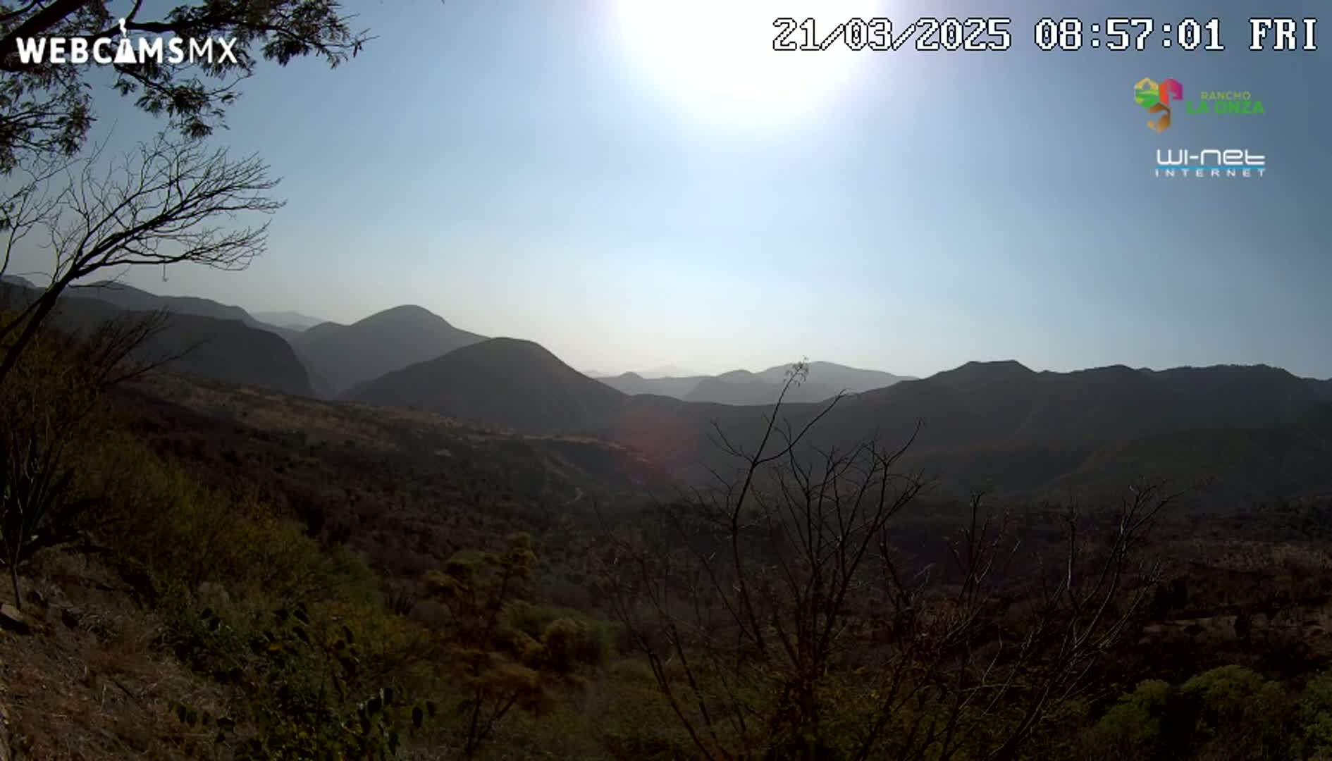A sunny day reveals a mountainous landscape, with scrubby vegetation covering the hillsides in the foreground.