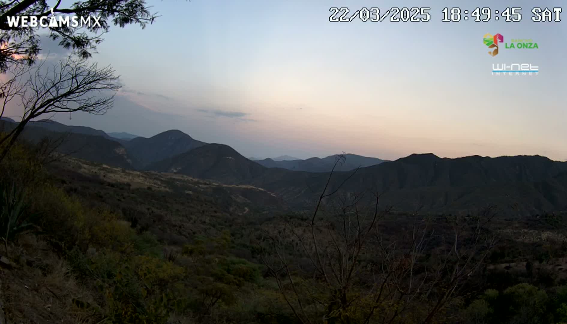 A dusky pink sunset illuminates a mountainous landscape of dark hills and valleys covered in low, scrubby vegetation.