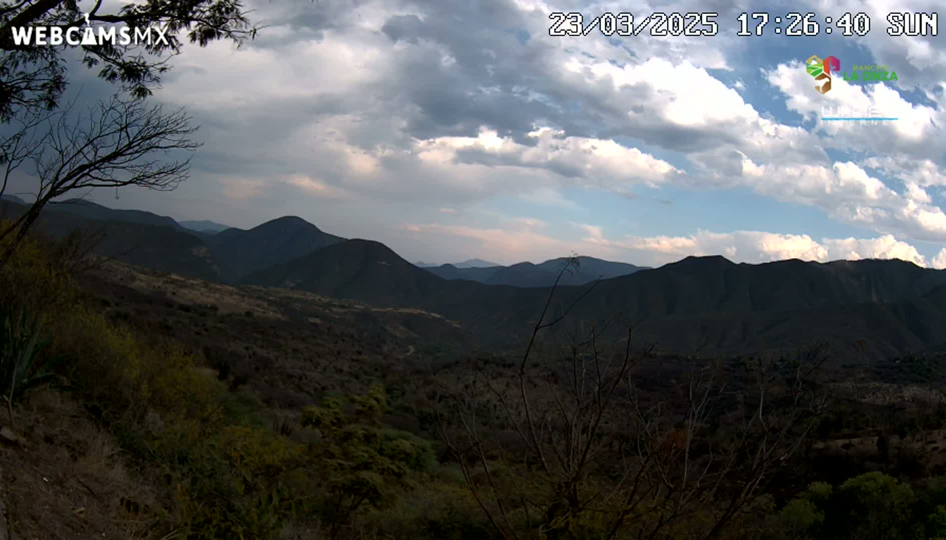 A partly cloudy afternoon view of a mountainous landscape with dry, scrubby vegetation.