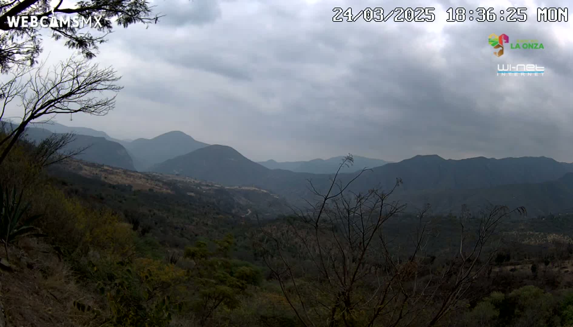 A view of a mountainous landscape under a cloudy sky shows a valley filled with dark green vegetation.