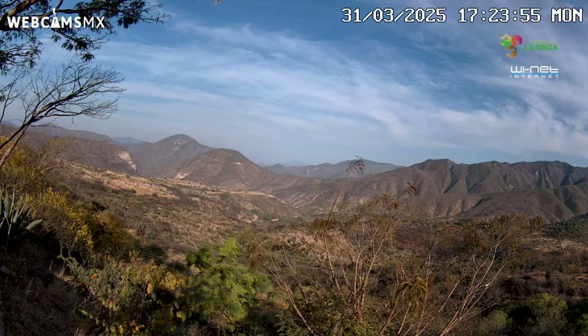 A partly sunny day reveals a view of a mountainous valley with sparse, dry-looking vegetation.