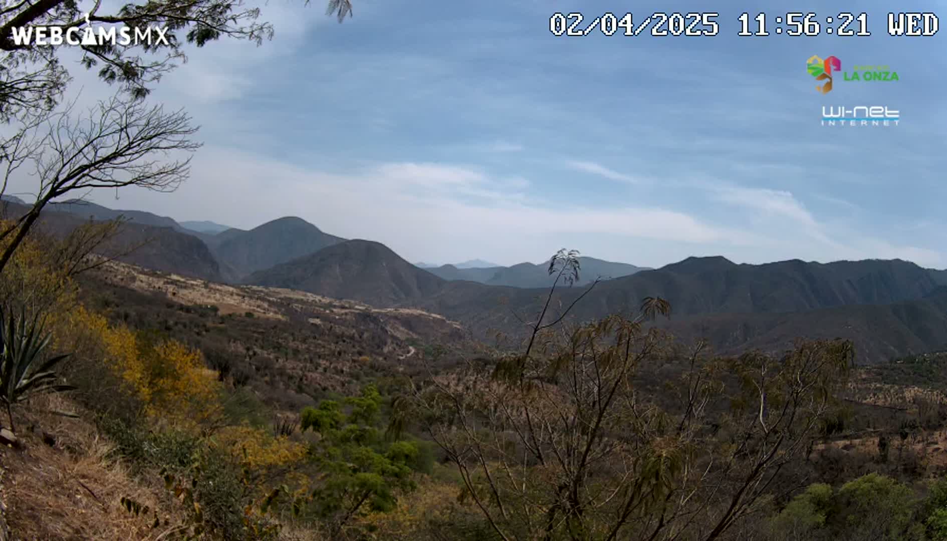 A partly cloudy sky overlooks a mountainous, dry landscape with sparse vegetation.