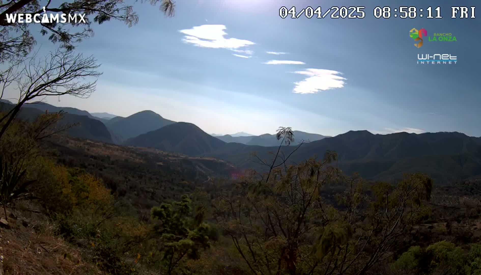 A mostly sunny, high-angle view shows a mountainous landscape covered in scrubby vegetation under a mostly clear sky.