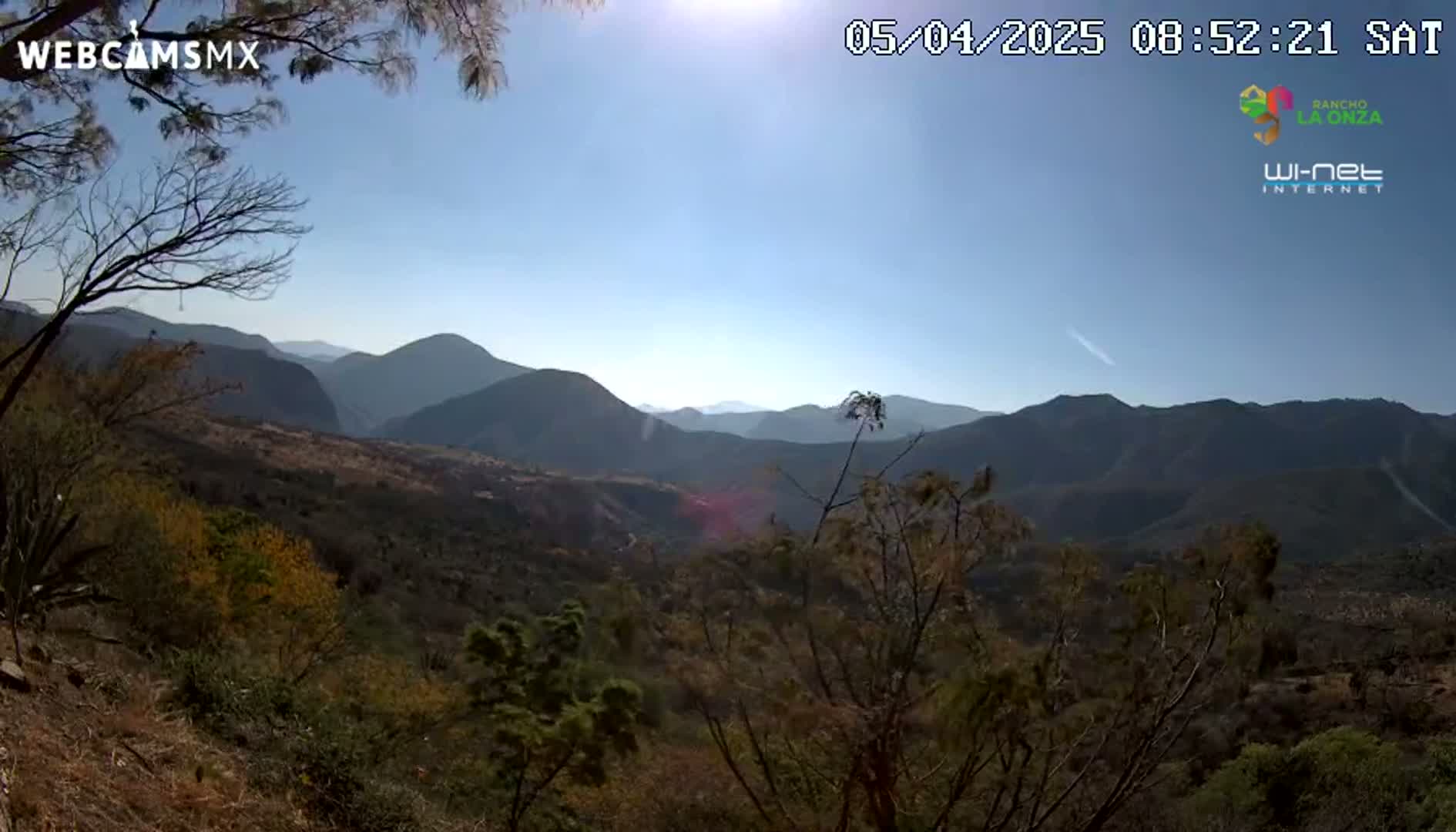 A sunny, clear day reveals a panoramic view of a mountainous landscape with dry, scrubby vegetation in the foreground.