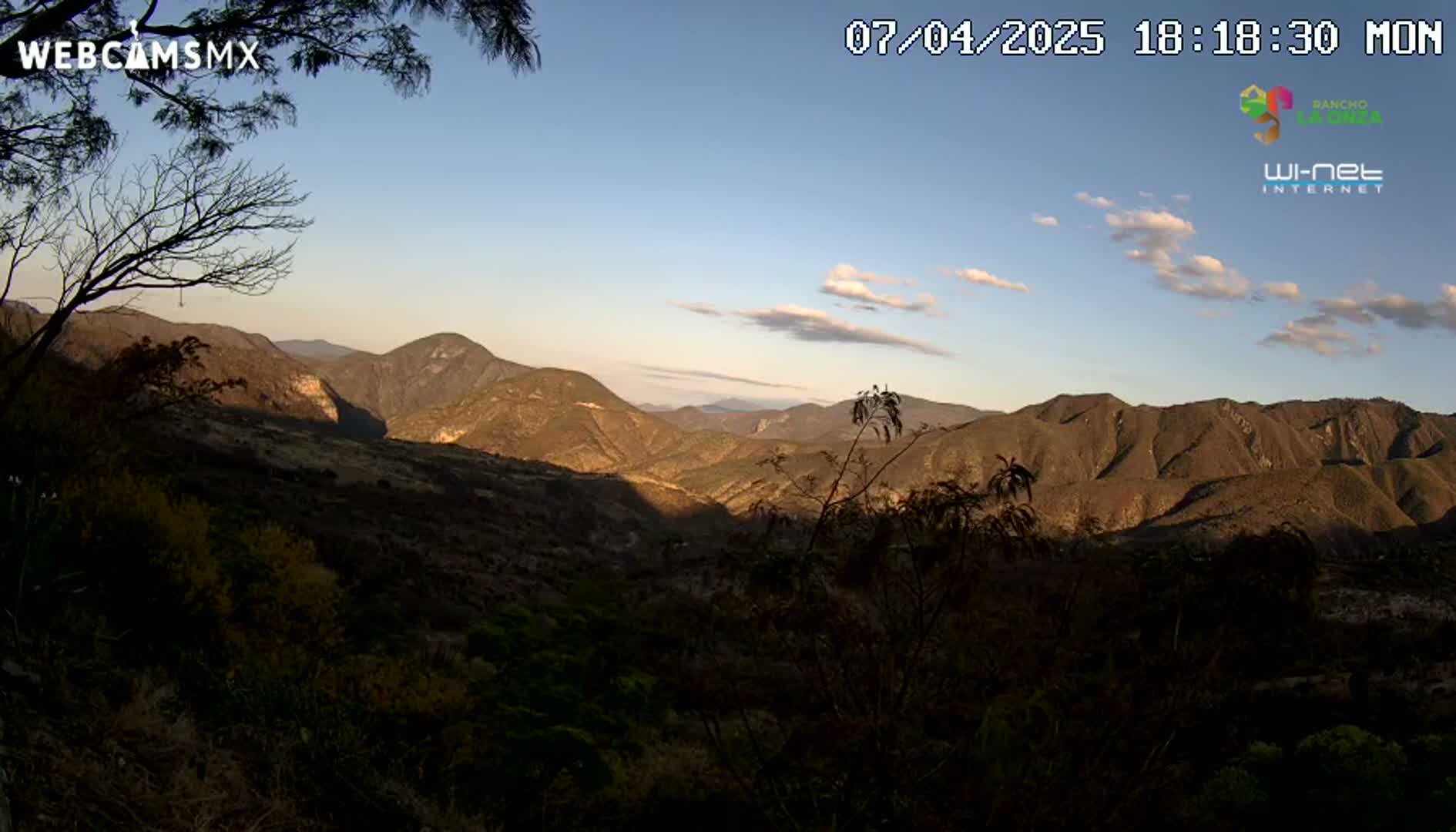 A mountain range is visible at sunset under a mostly clear sky with a few scattered clouds.