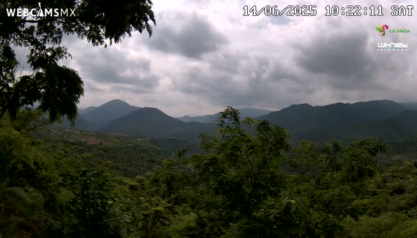 A lush, green, mountainous landscape is viewed from an elevated position under a cloudy sky.