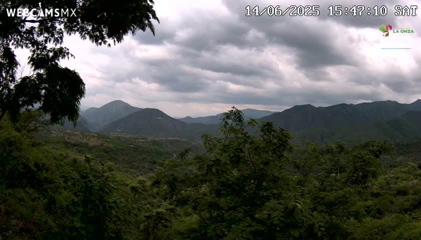 A lush, green, mountainous landscape is viewed from an elevated position under a cloudy sky.