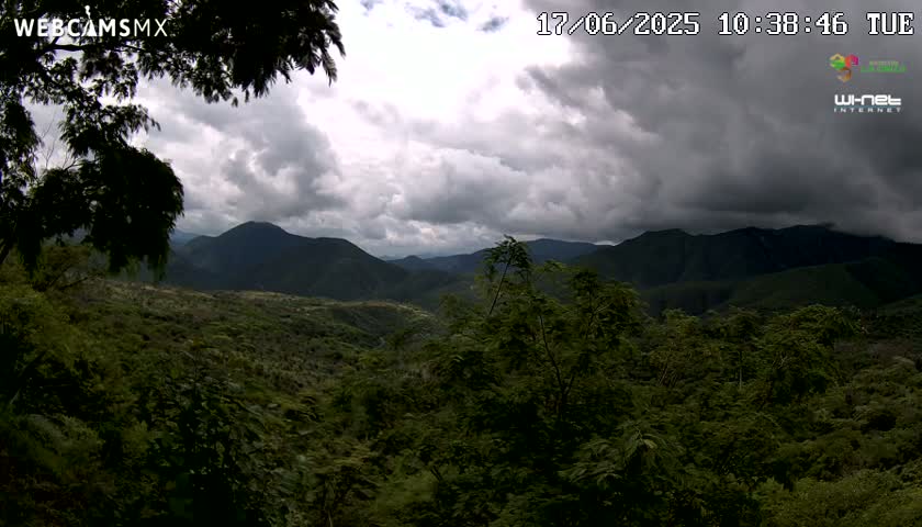 A lush, green mountain range is visible under a cloudy sky.
