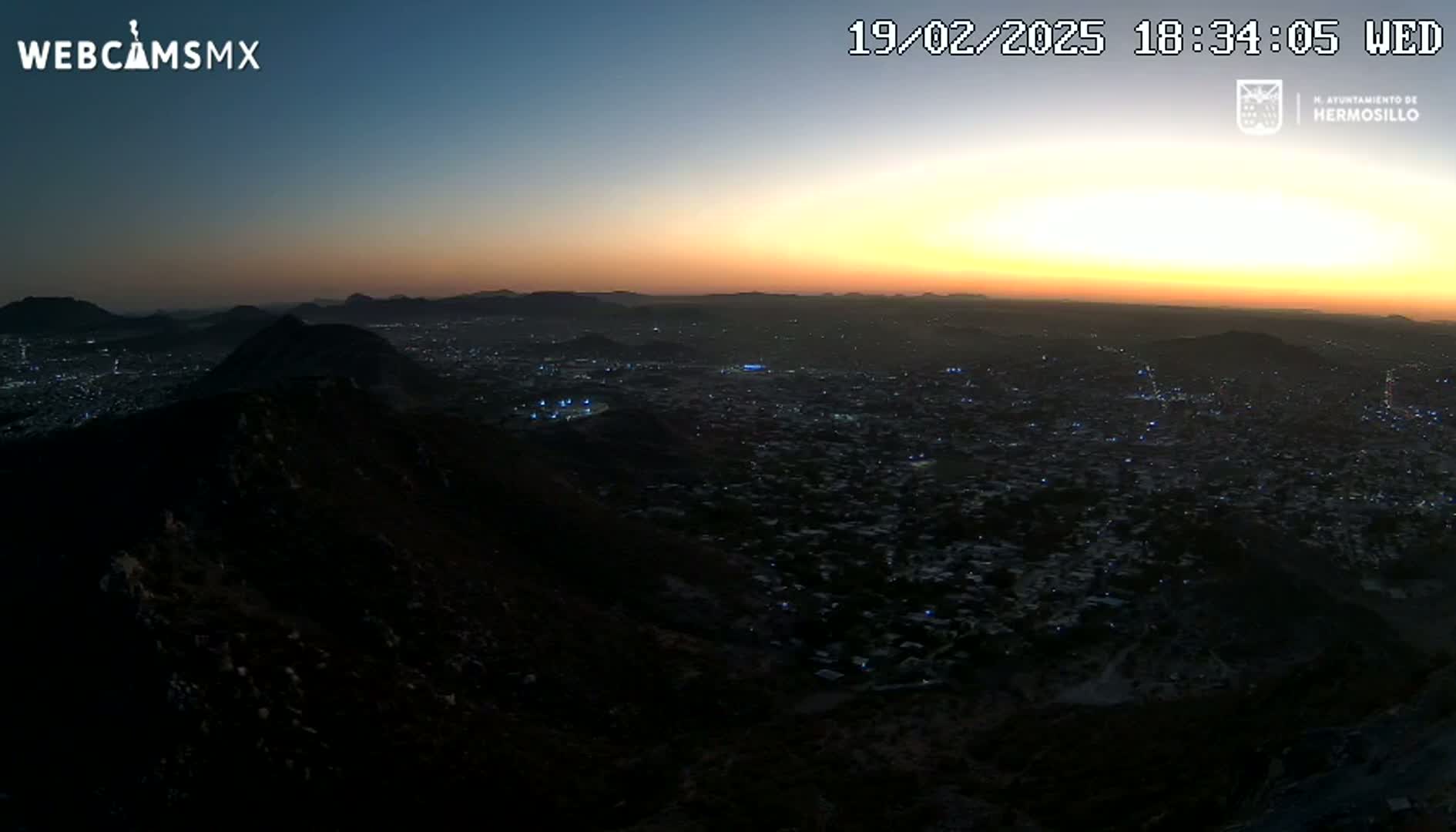 A nighttime view from a mountain overlooking a city during a sunset with a clear sky.