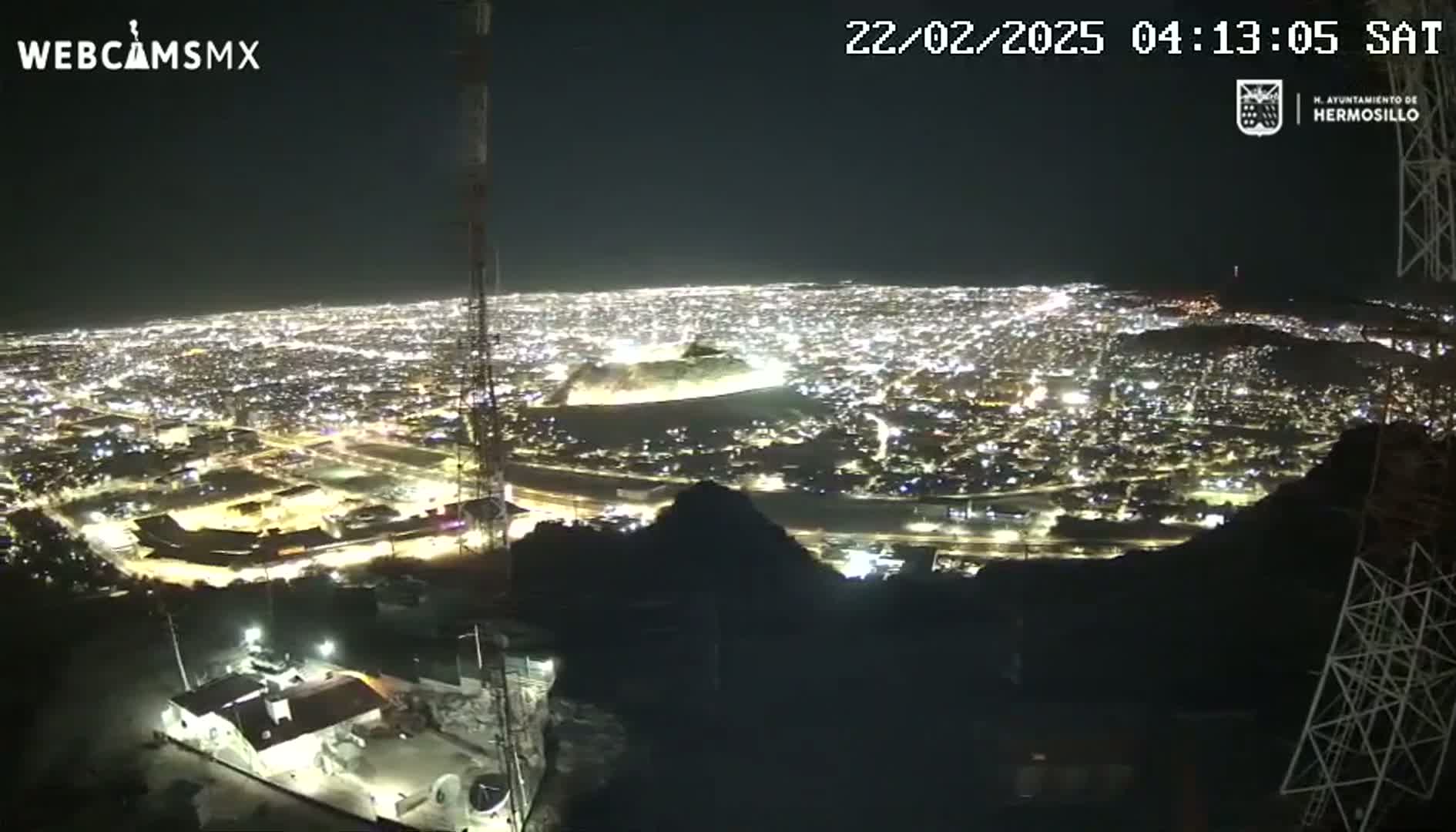 A nighttime, high-angle view of a city illuminated by numerous lights, seen from a vantage point on a hill or mountain.