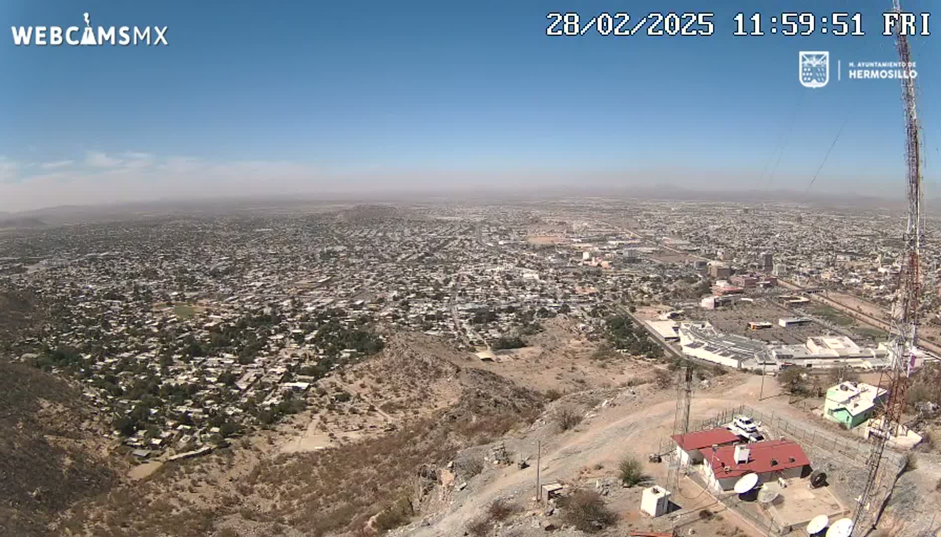 A sprawling city is visible from a hilltop on a hazy, sunny day.