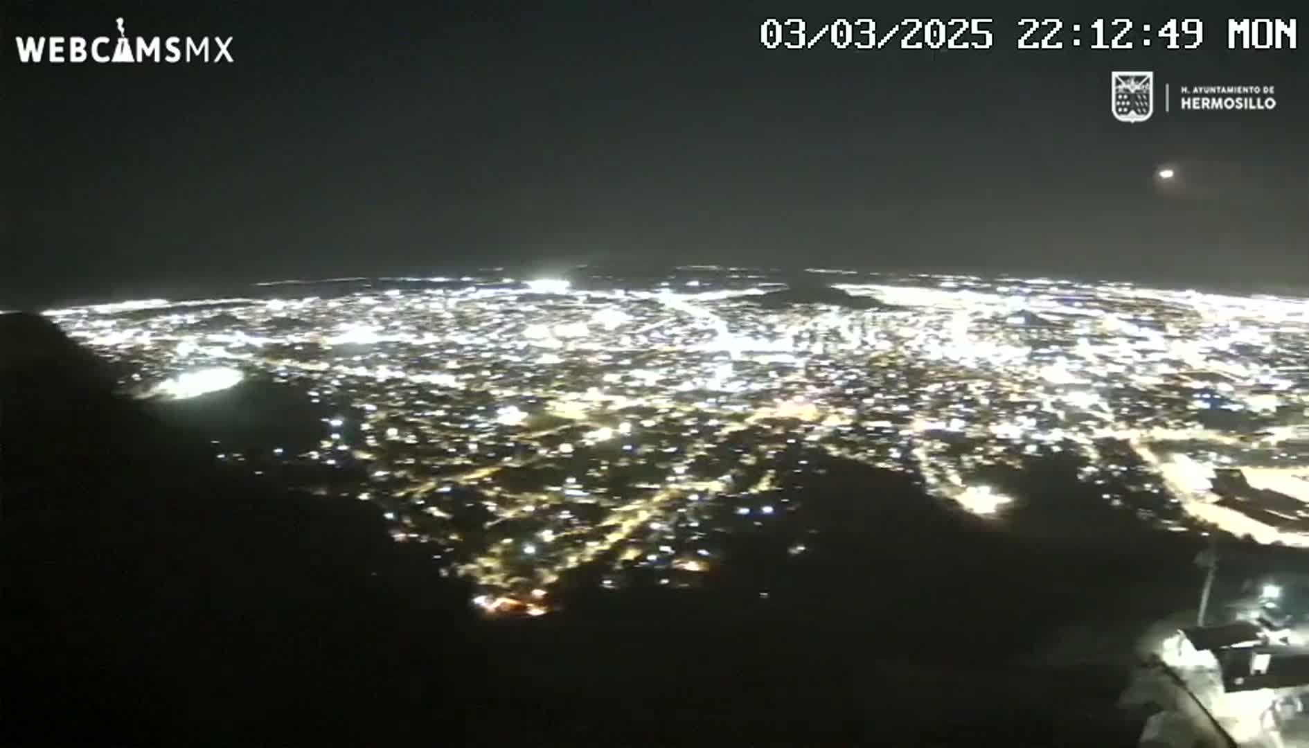 A nighttime, aerial view shows a sprawling city illuminated by countless lights.