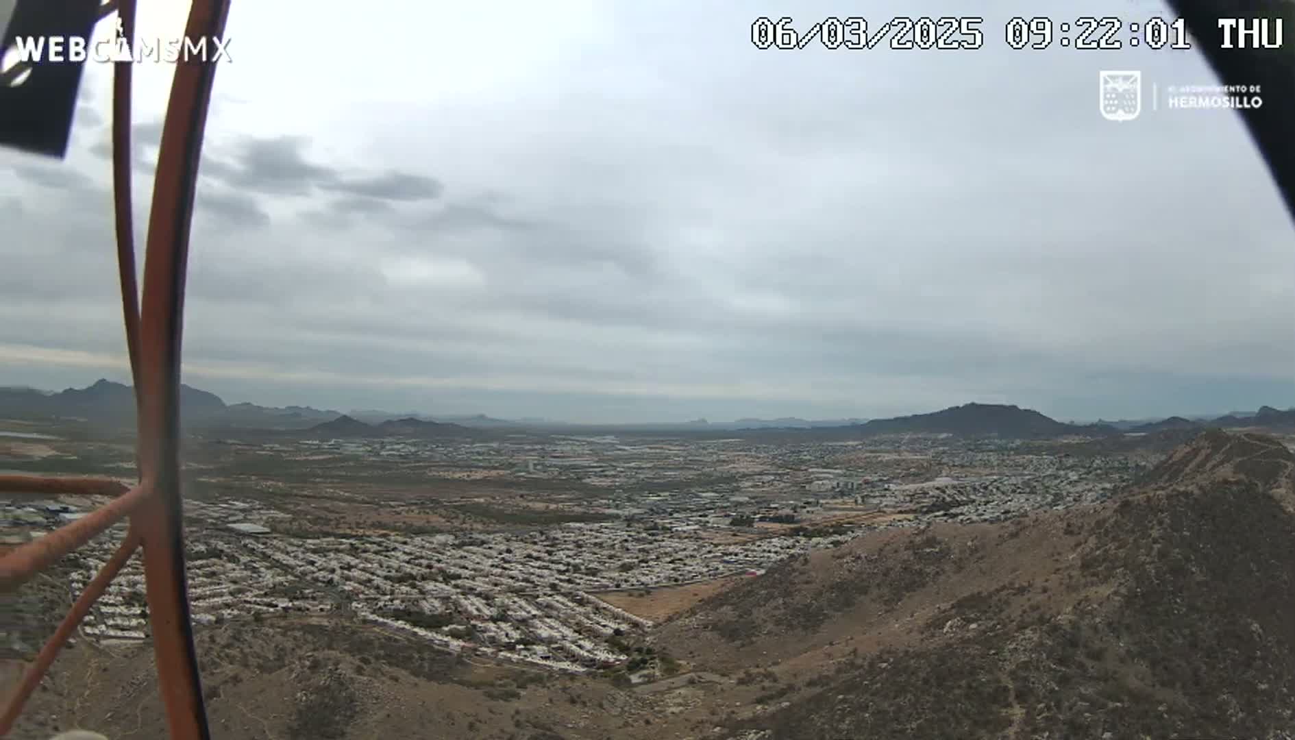 A sprawling city is visible from a hilltop vantage point under an overcast sky.