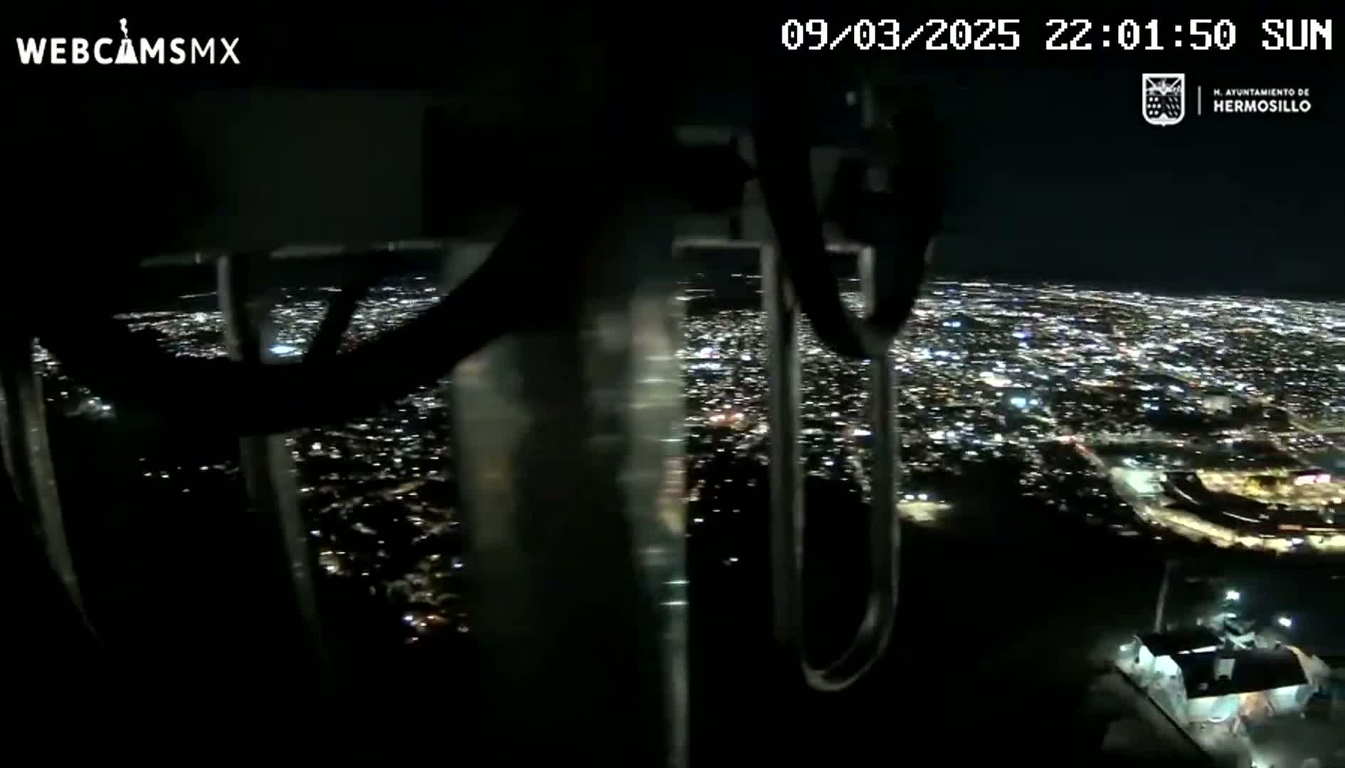 A nighttime, high-angle view shows a sprawling city illuminated by countless lights.