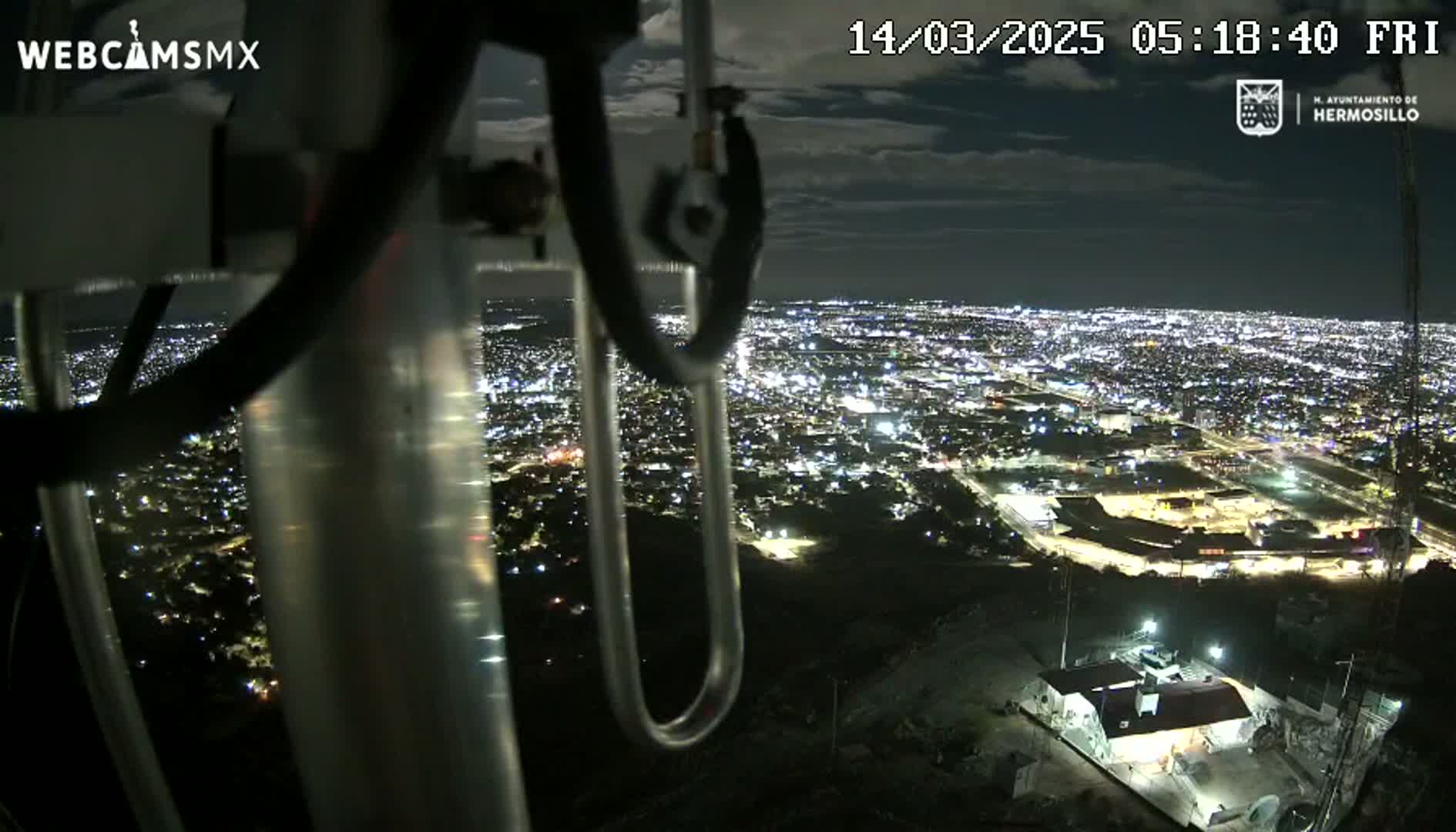 A nighttime view from a tall structure shows a sprawling city illuminated below under a partly cloudy sky.
