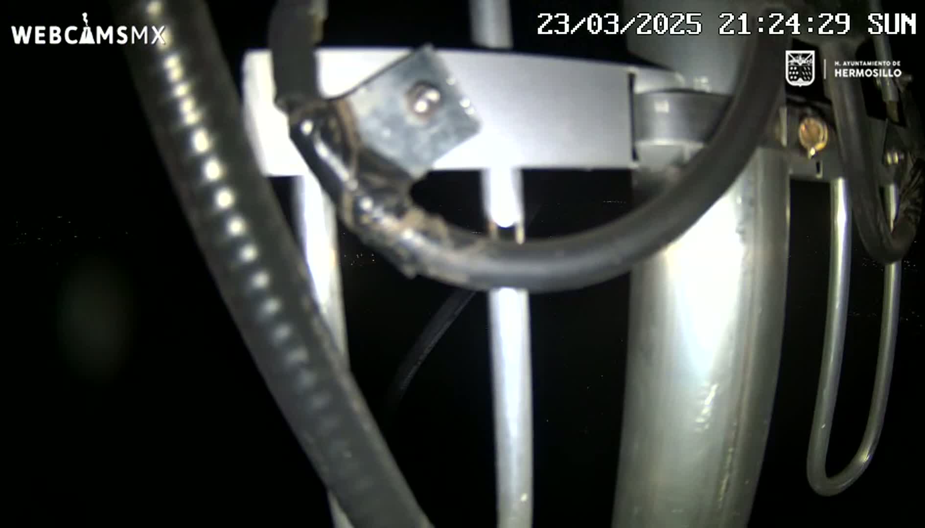 A close-up nighttime view of a metallic structure with several black cables and wires attached.