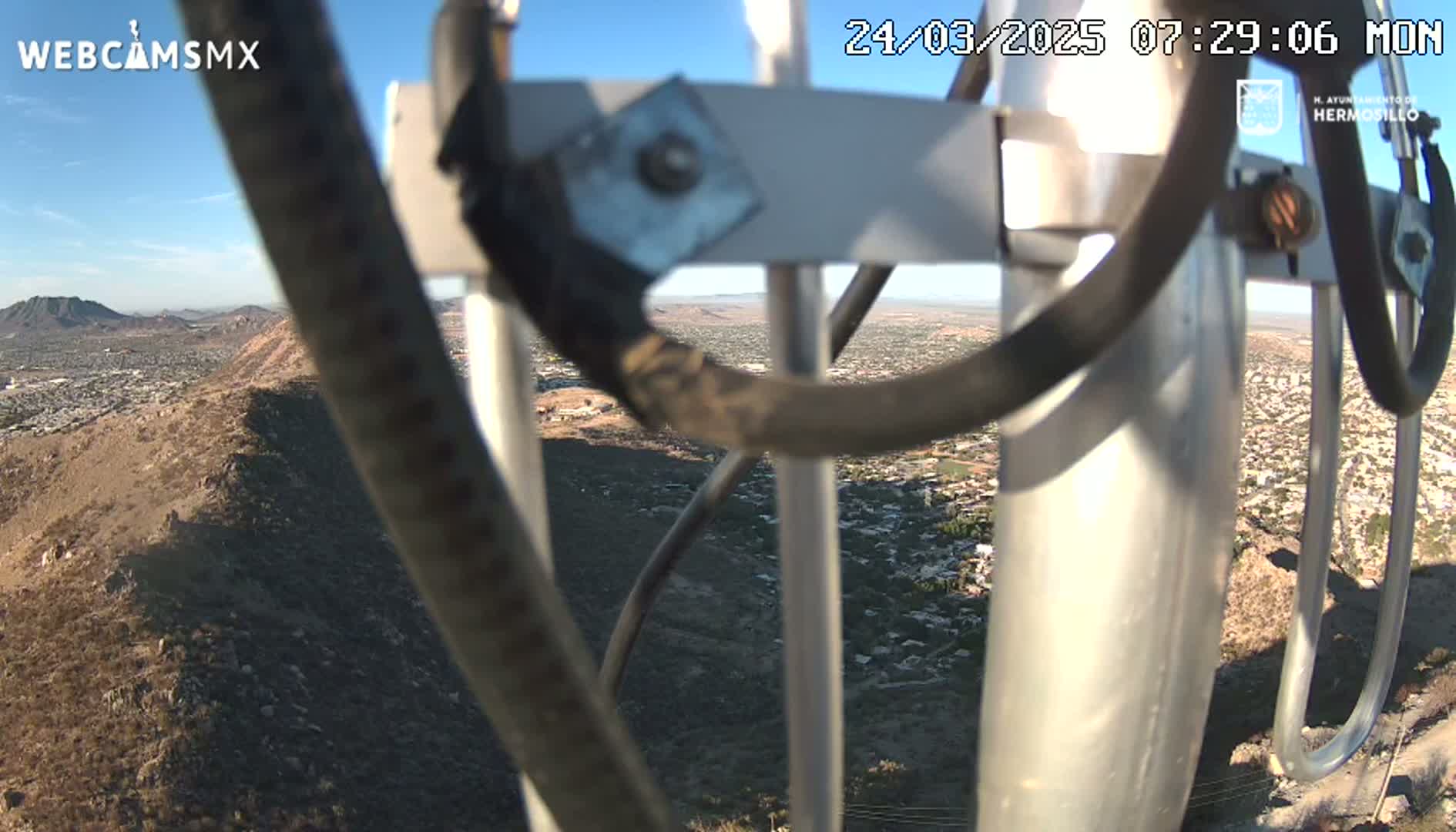 A view of a city and surrounding desert landscape on a clear, sunny day, seen through the metal framework of a tall structure.
