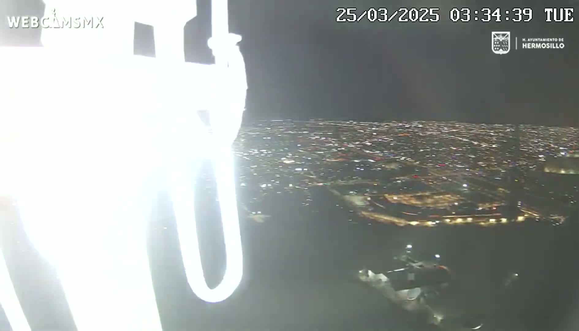A nighttime aerial view of a sprawling city illuminated by countless lights, observed from what appears to be a tall structure or vehicle.