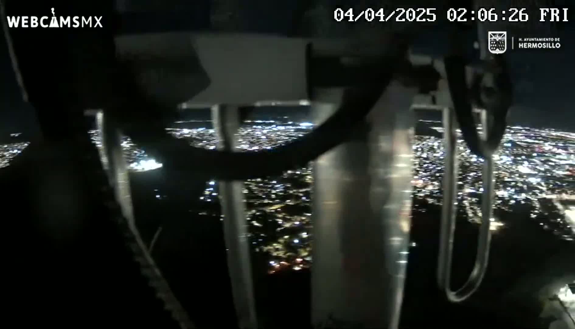 A nighttime view of a city's lights from a tall structure, seen through a metal framework.