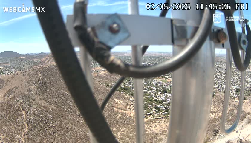 A view from a tall structure on a clear, sunny day shows a sprawling desert town below and a rocky, brown hillside in the foreground.